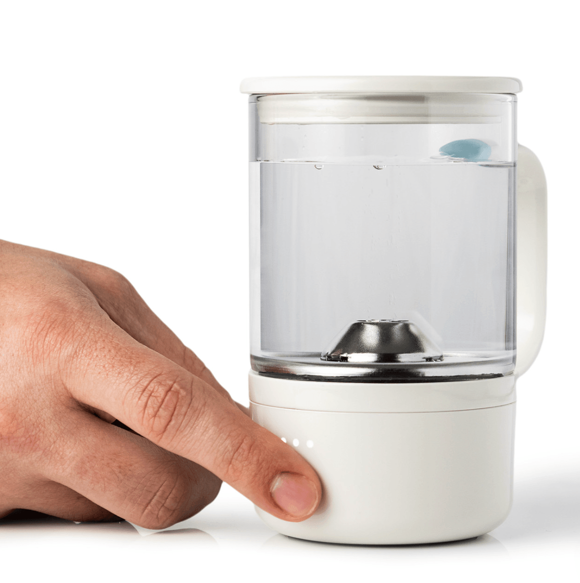 Hand pressing a button on a white automatic pet water fountain with a transparent water container and blue water filter inside.