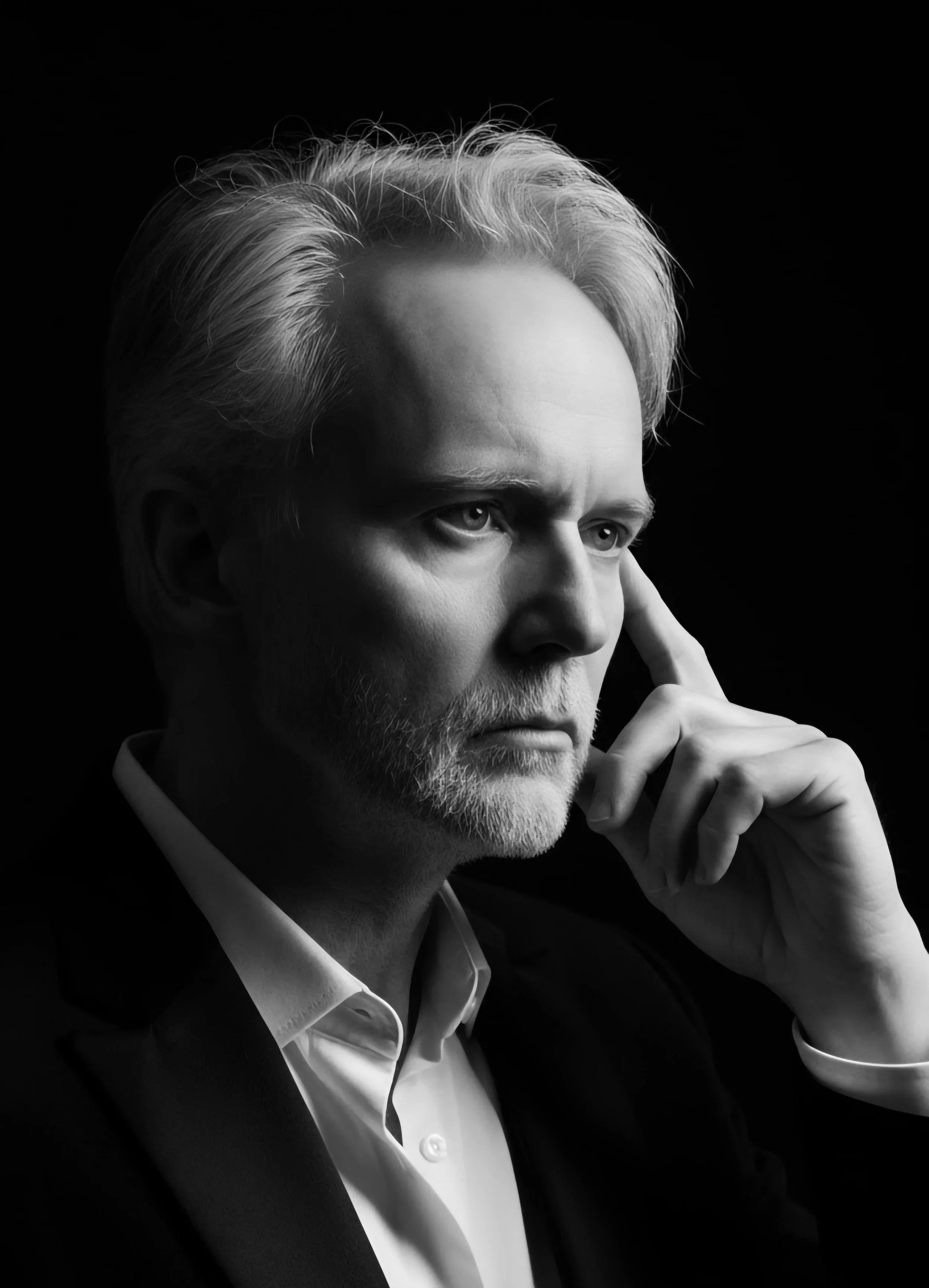 Black and white portrait of healer Brian Collins "The Rabid Monk" with gray hair and beard, wearing a suit and white shirt, gazing thoughtfully to the right with his hand resting near his temple.