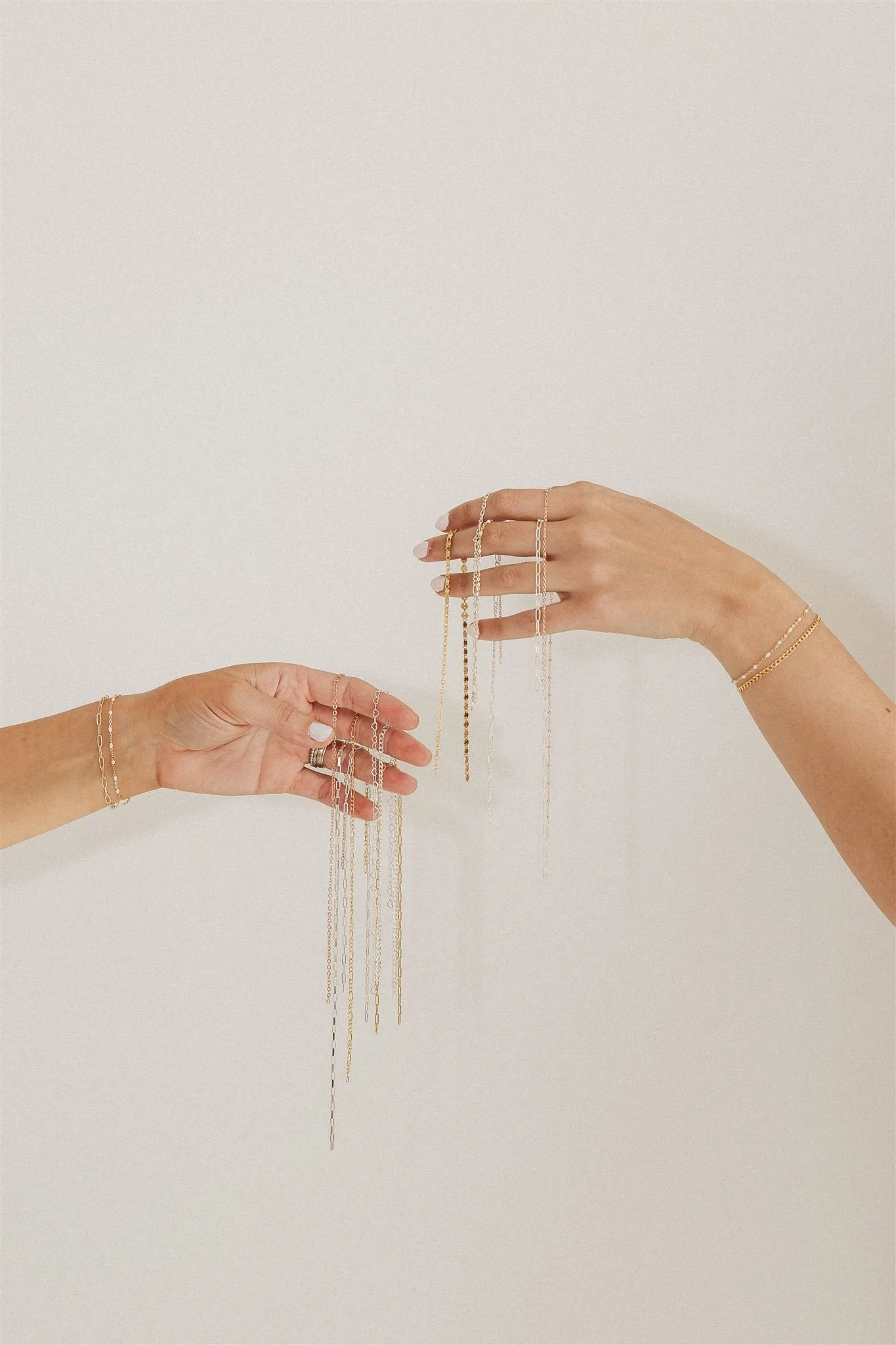 Two hands displaying multiple delicate gold and silver jewelry chains against a plain white background.