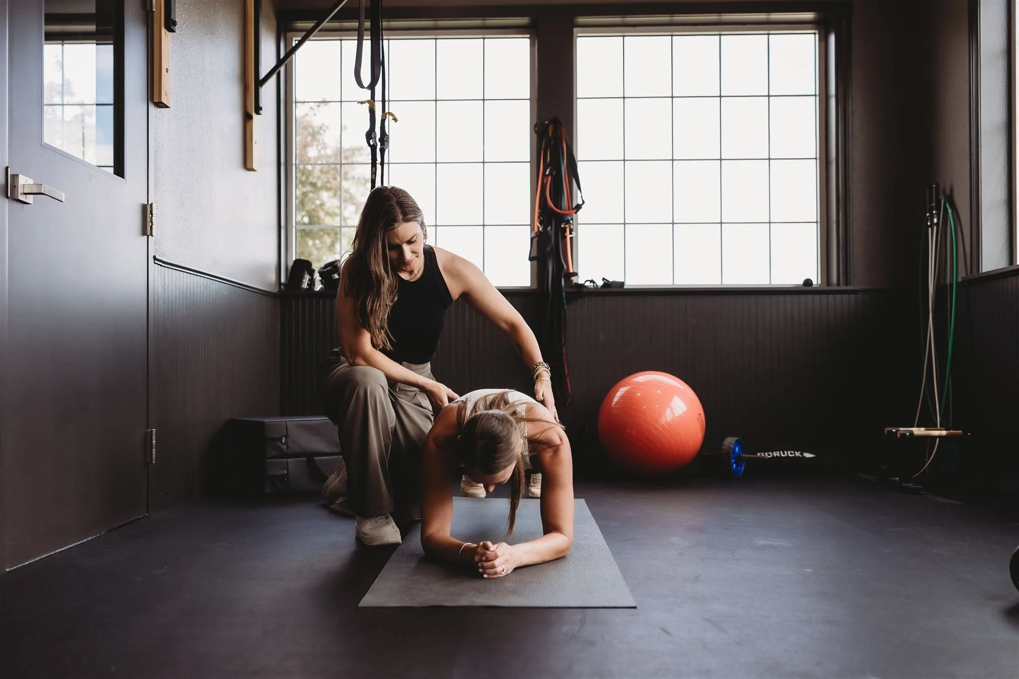A Vitality Physical Therapy and Wellness physiotherapist guiding a patient through a supported core rehabilitation exercise on a yoga mat in a gym setting