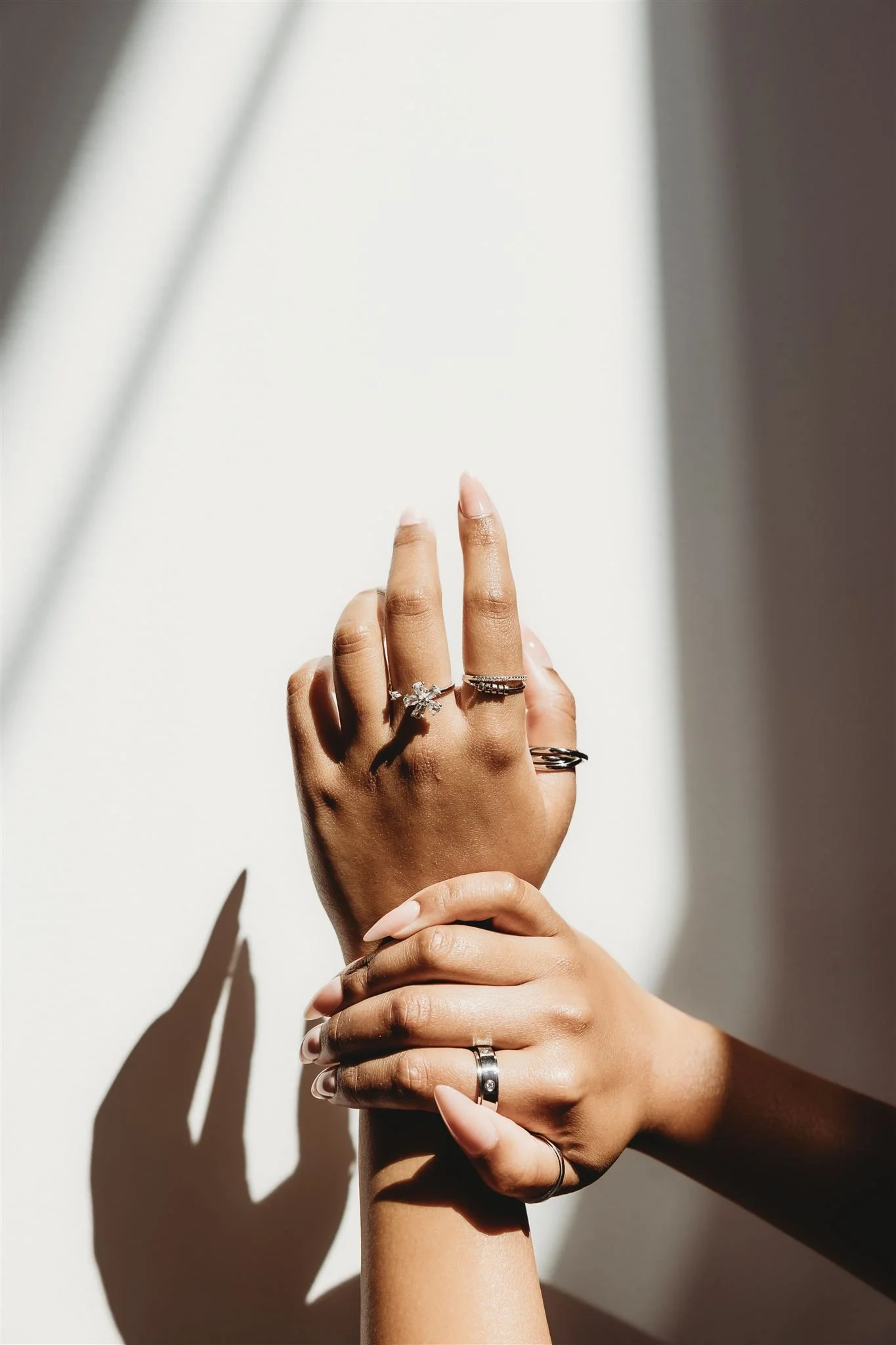 Close-up of a person's hand with multiple rings, held upright against a plain background with sunlight and shadows.
