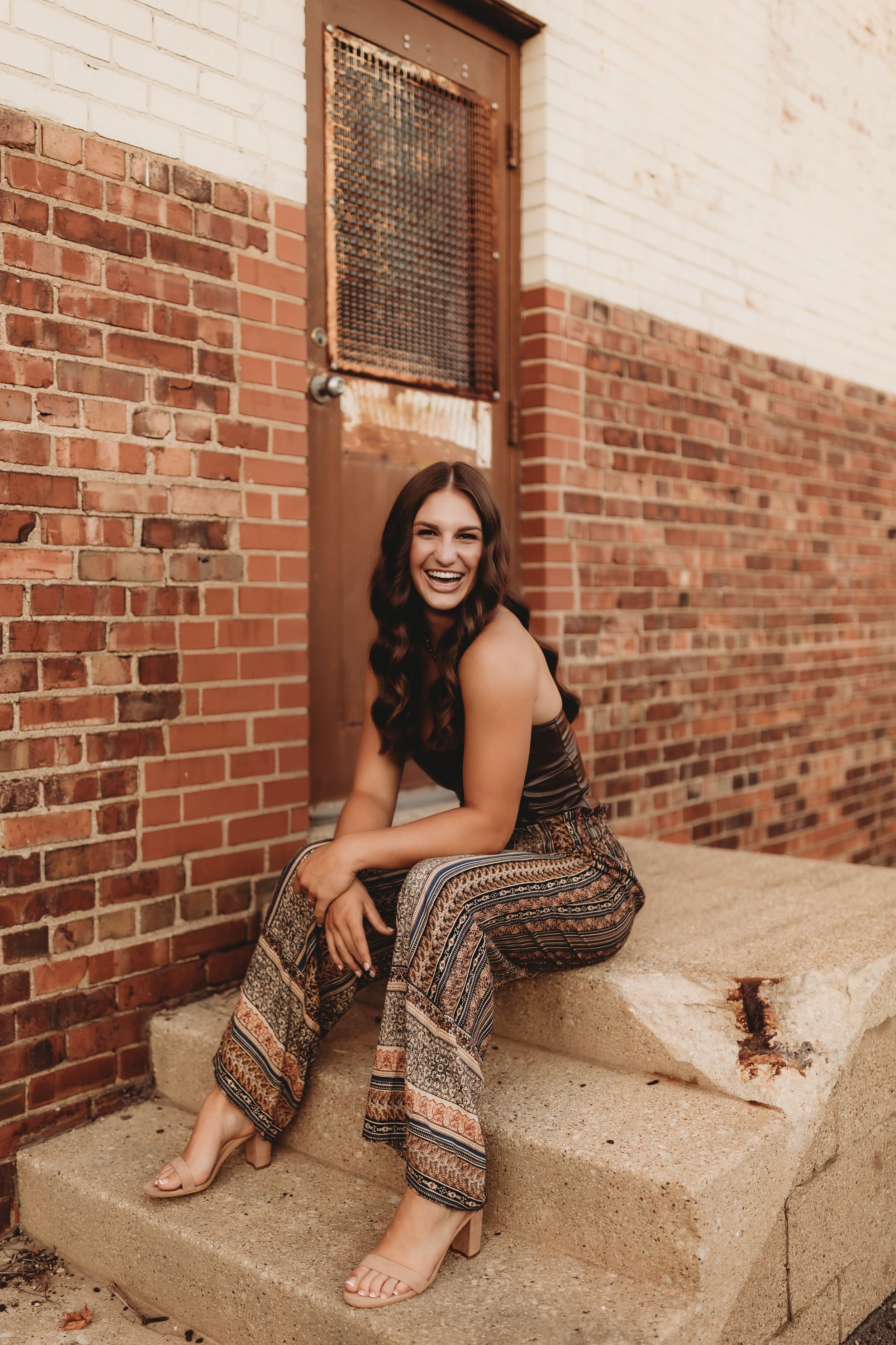  Metamora senior sits on a set of steps in front of a brick wall and smiles while testing senior picture ideas 