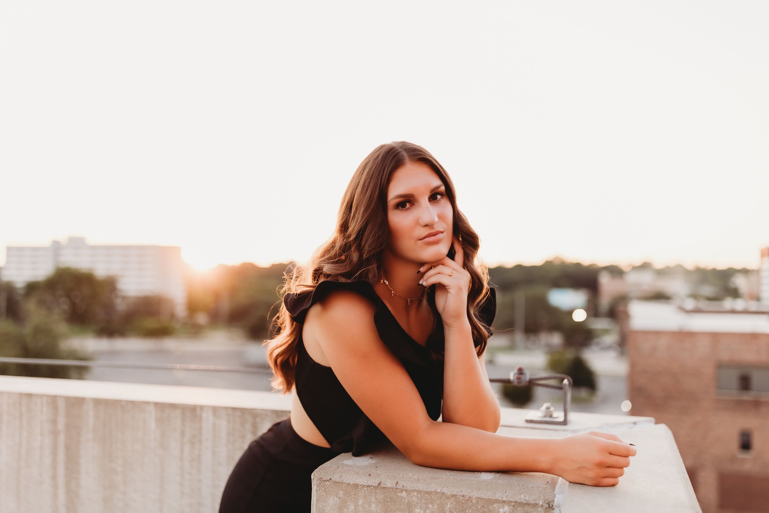  High school senior stands on a downtown peoria rooftop and rests her face on her hand as she leans on the edge while posing for senior picture ideas 