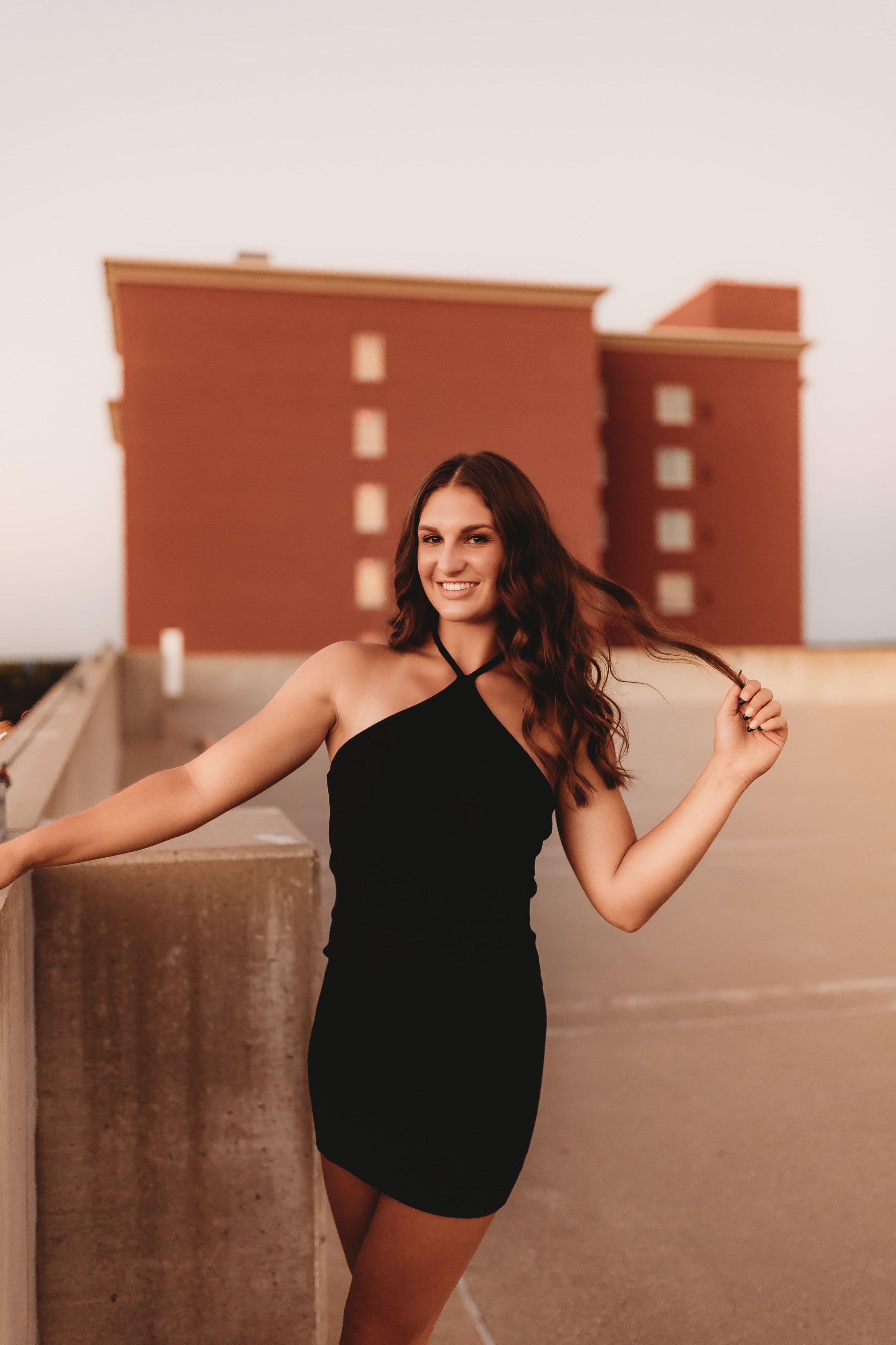  High school senior stands on top of a peoria rooftop with one hand on the edge of the roof and another holding a strand of her hair while posing senior photographers near me 