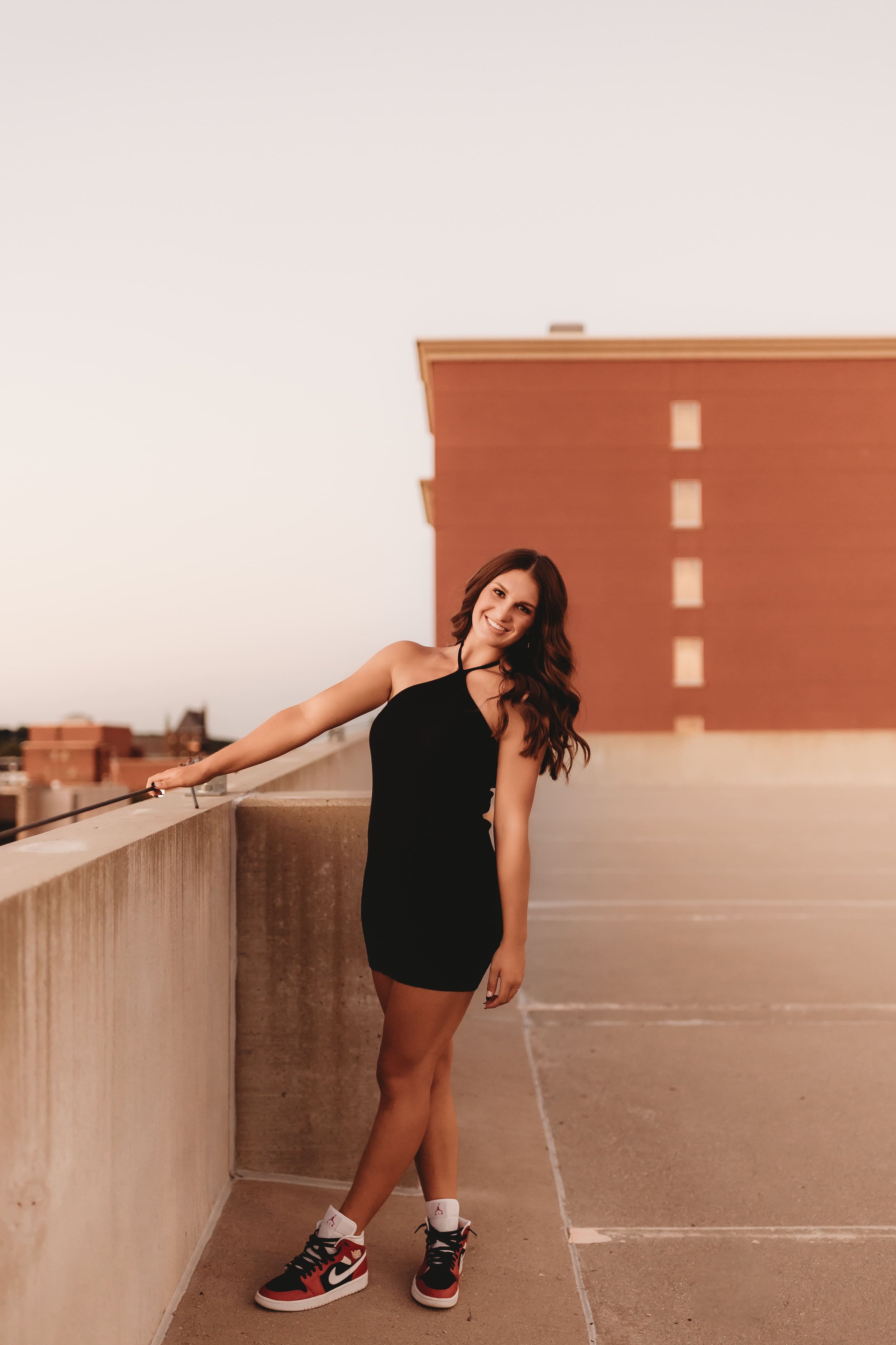  While posing for senior photographers near me, Katy leans away from the edge of a downtown peoria rooftop while smiling 