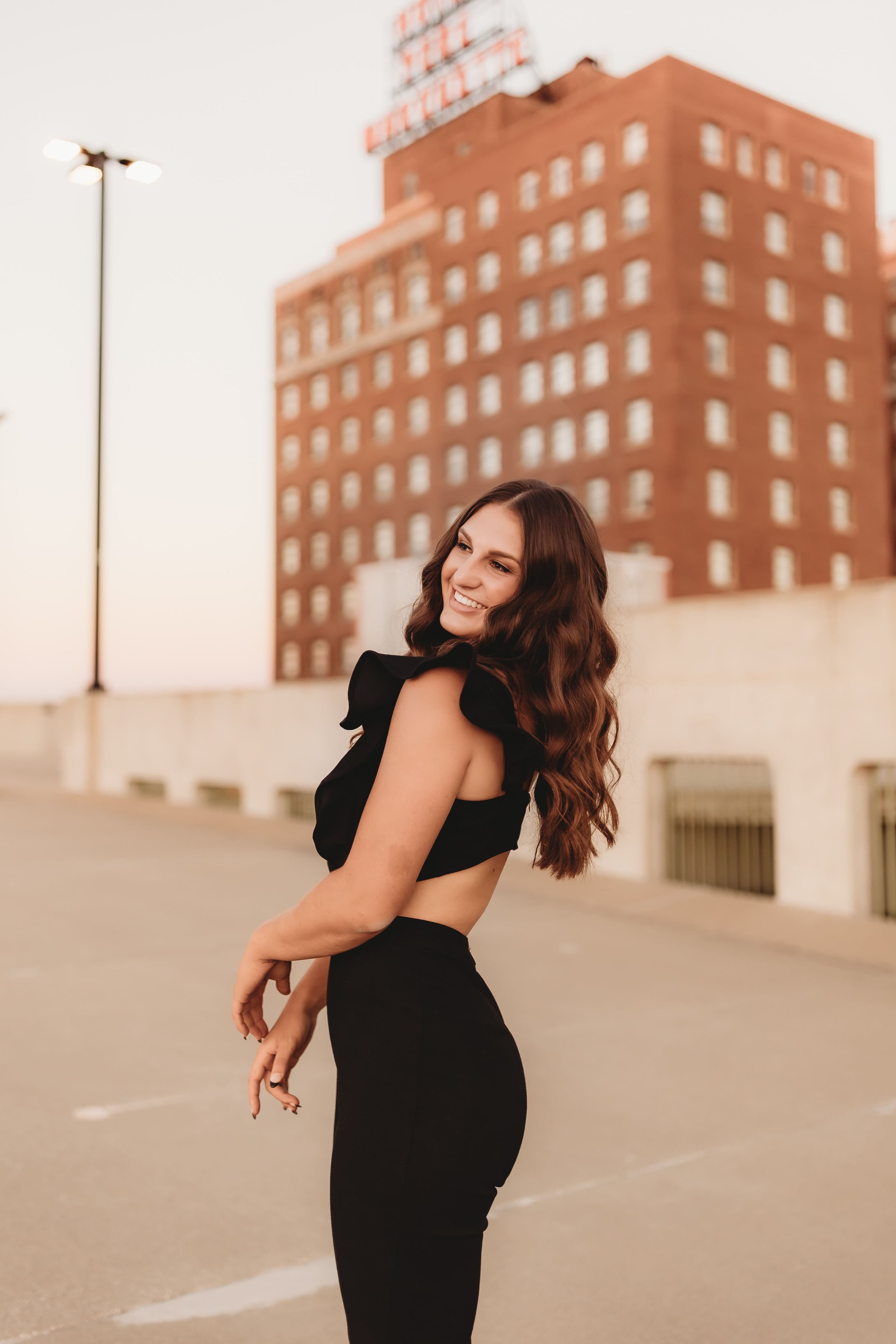  High school senior stands on a peoria rooftop and smiles while moving her arms while being captured by senior photographers near me 