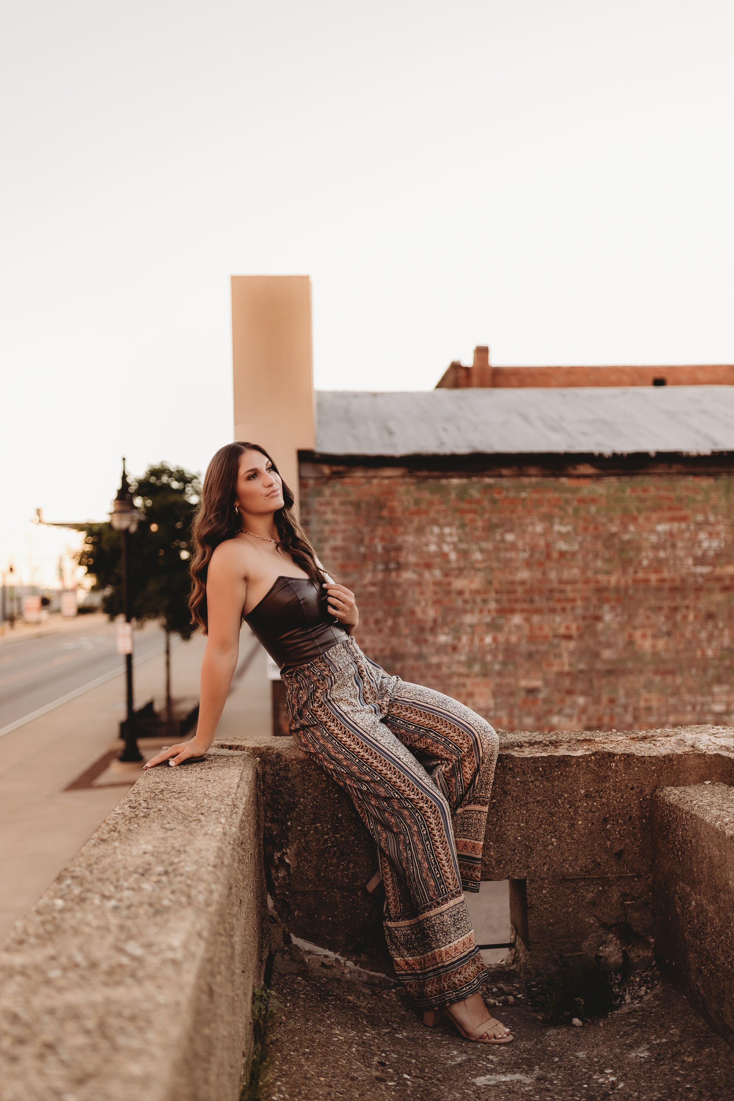  Metamora senior leans on the edge of a downtown peoria rooftop and looking off into the distance and posing for senior photographers near me 