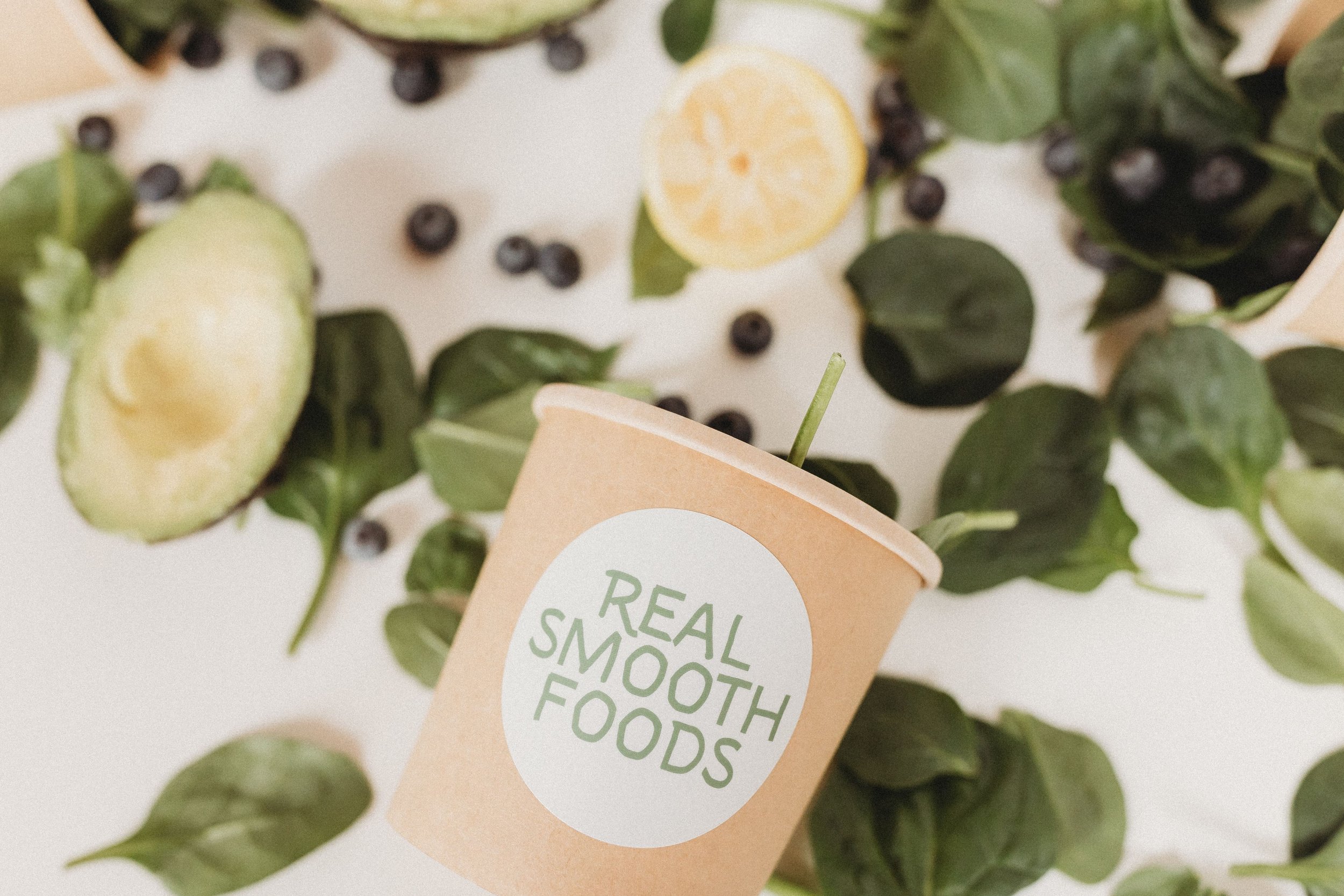  a real smooth foods cup lays out among spinach, blueberries, and an avocado 