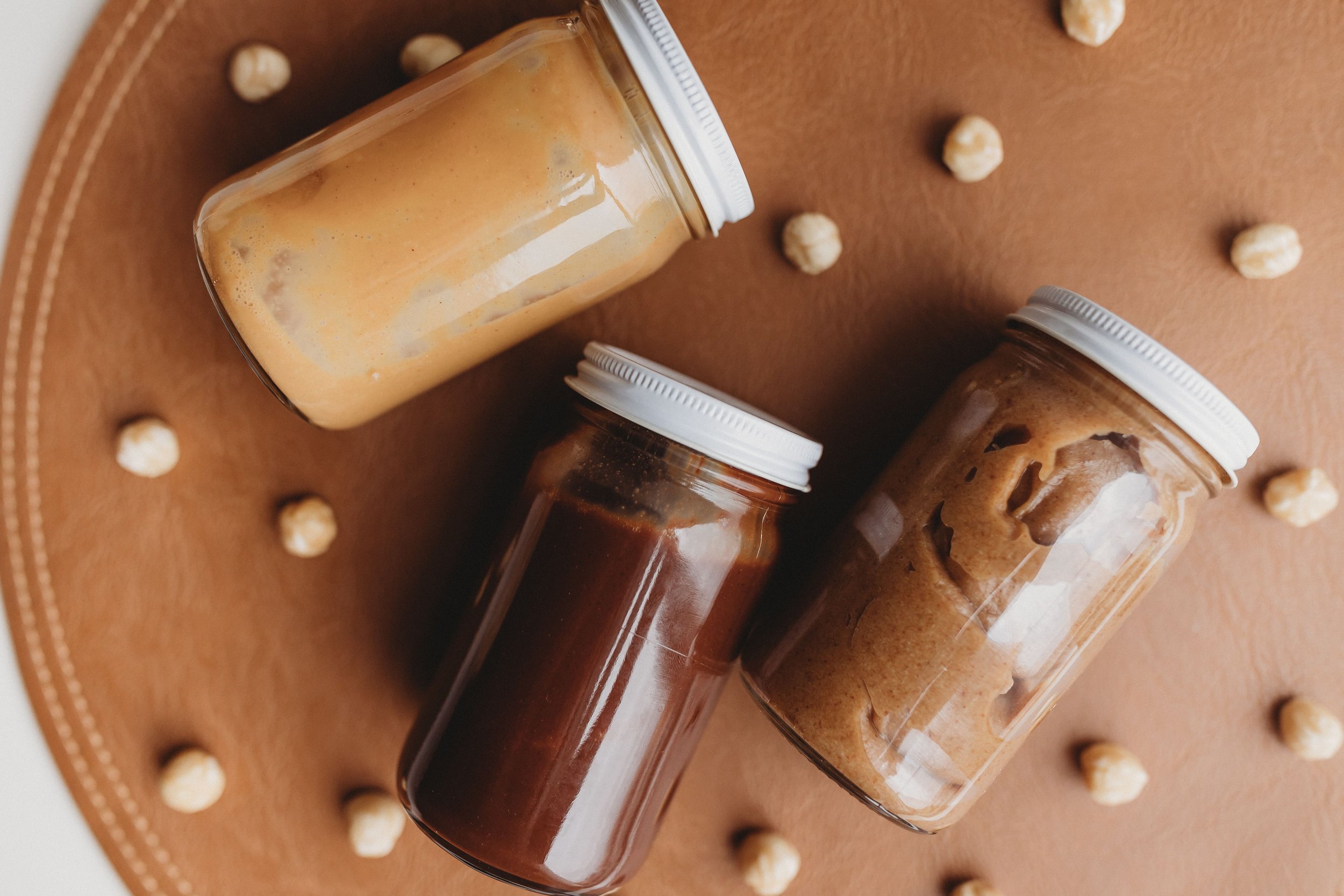  three jars of handmade spreads lay next to each other among hazelnuts 