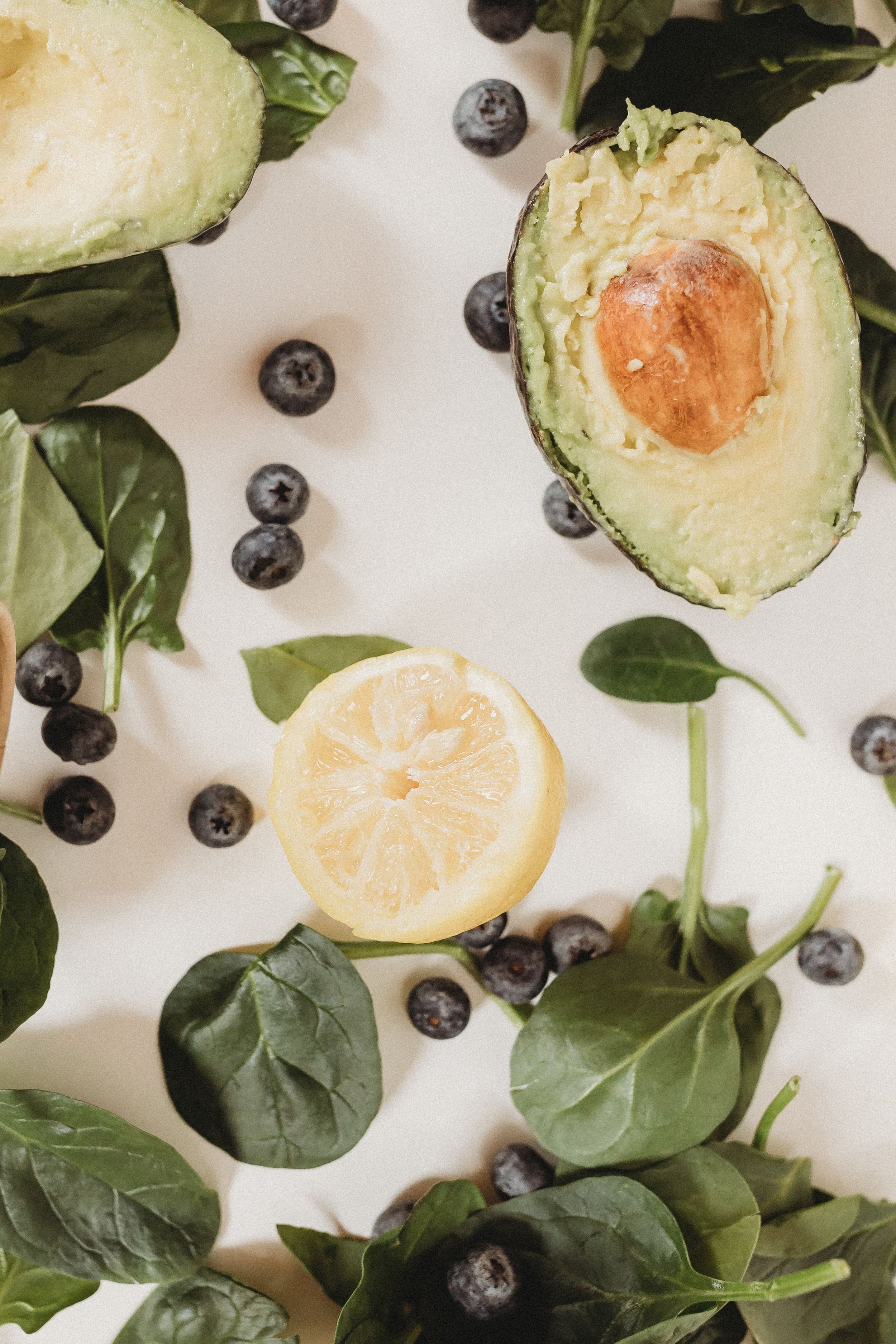  spinach and blueberries and lemons and avocados are scattered around a white backdrop during a professional food brand shoot 