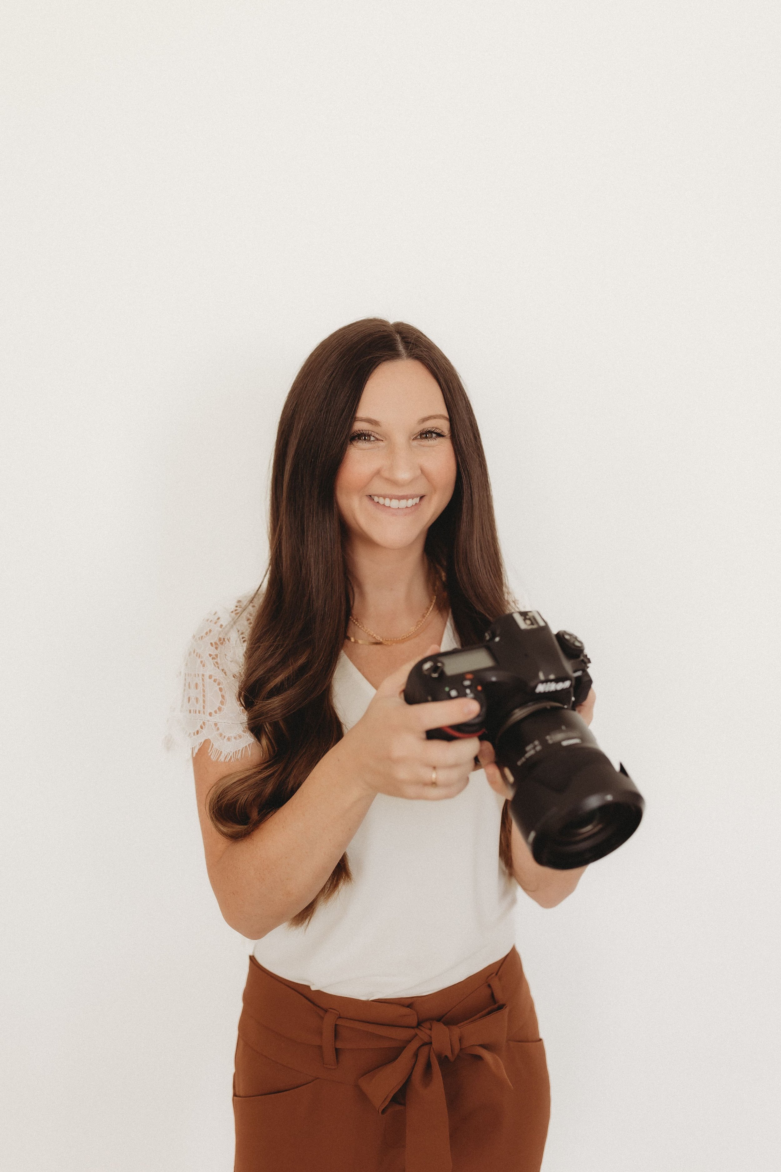  a woman smiles while holding a camera during realtor headshots 