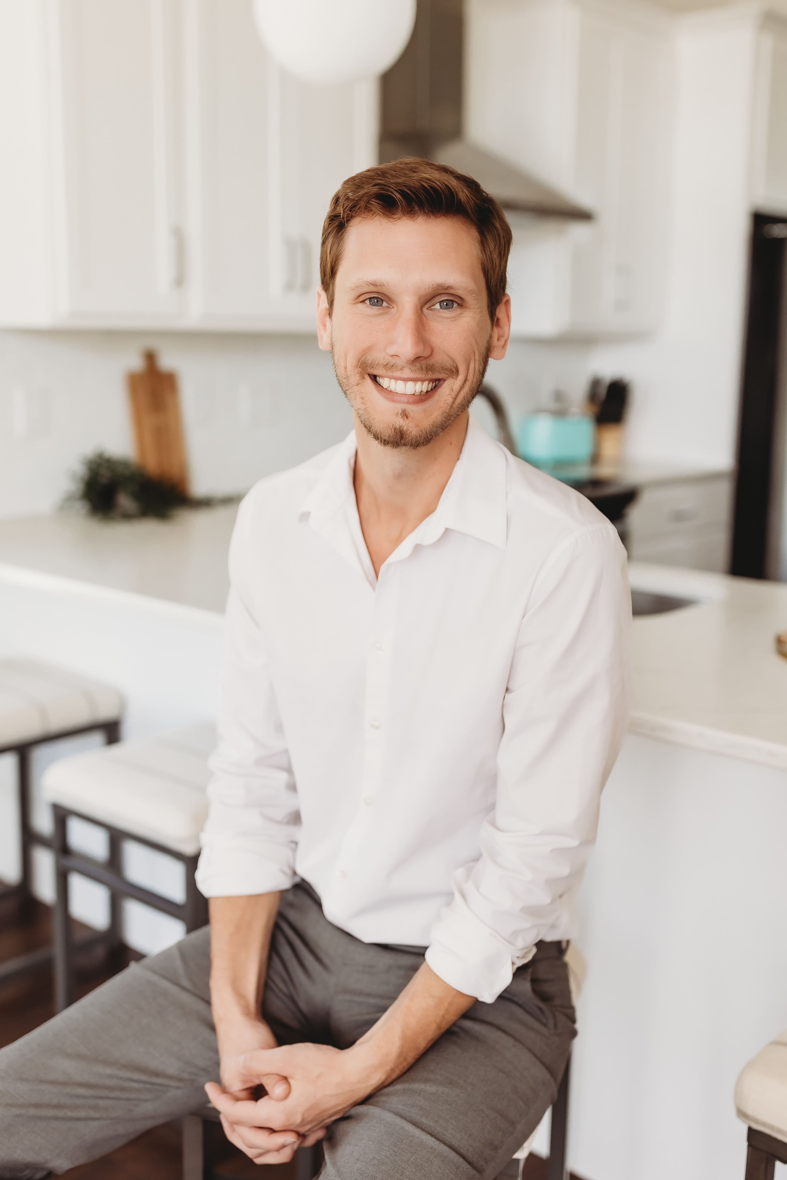  a man smiles wide while sitting on a stool in a bright kitchen for his realtor headshots 