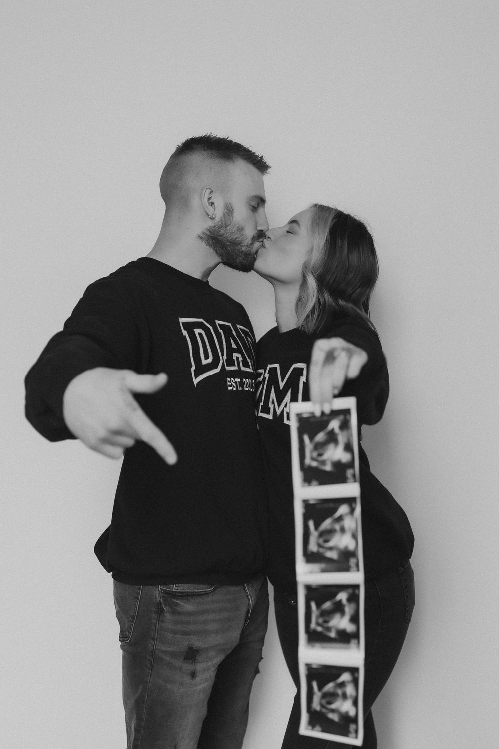  an expectant couple share a kiss as dad points to the sonogram photo 
