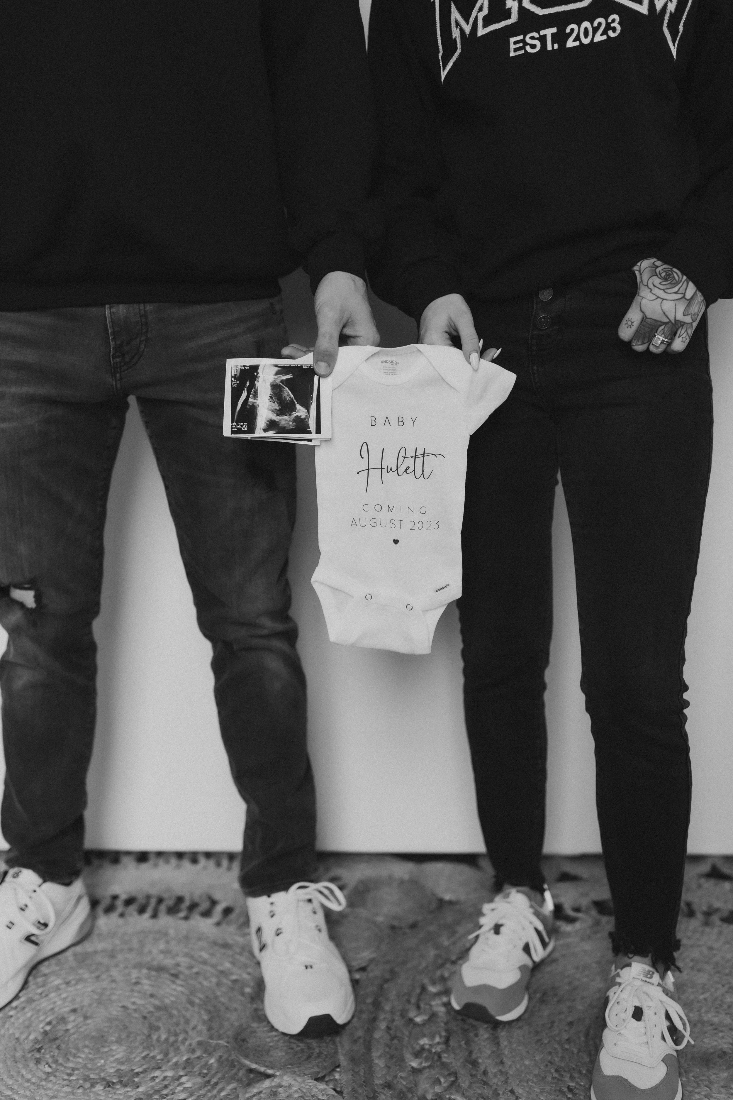  an expecting couple hold a sonogram photo and a onesie between them during a pregnancy announcement photoshoot 