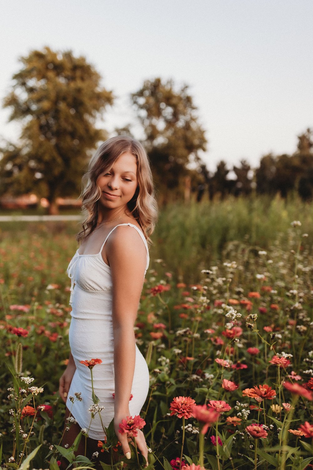  a high school senior wears a short white dress in a flower field during a session with a senior photographer near me 