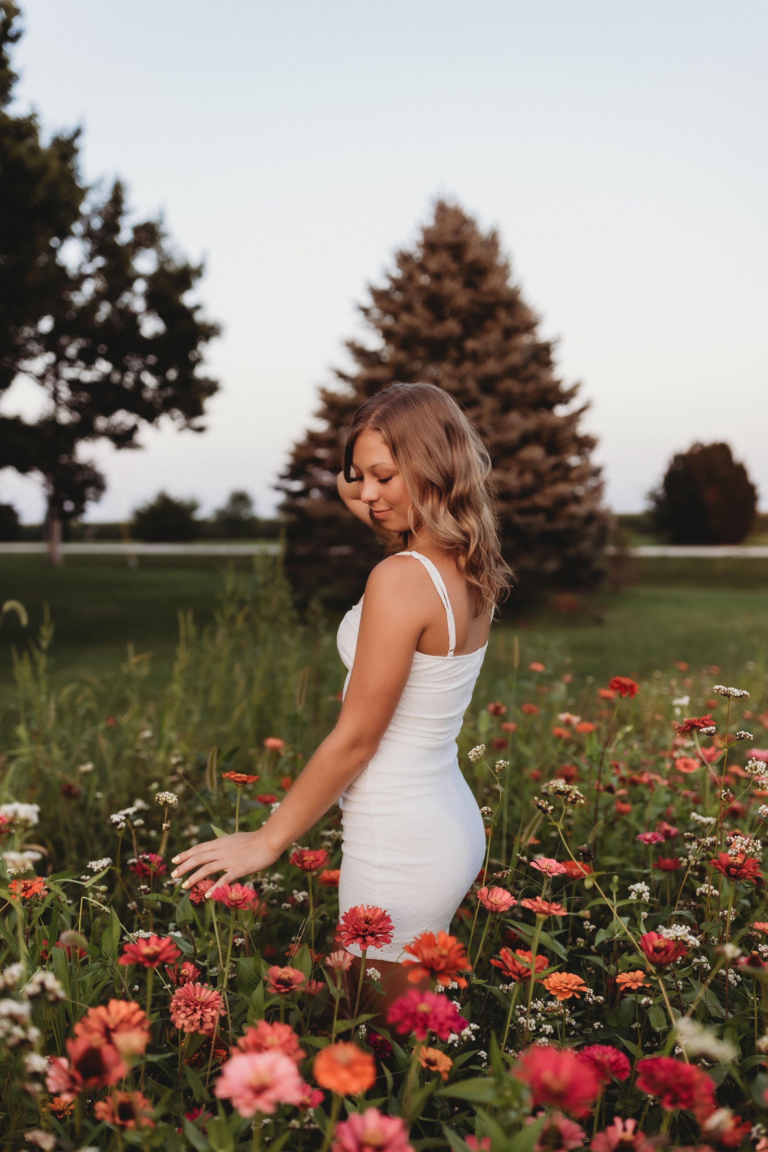  a young woman stands in a flower field wearing a white dress 
