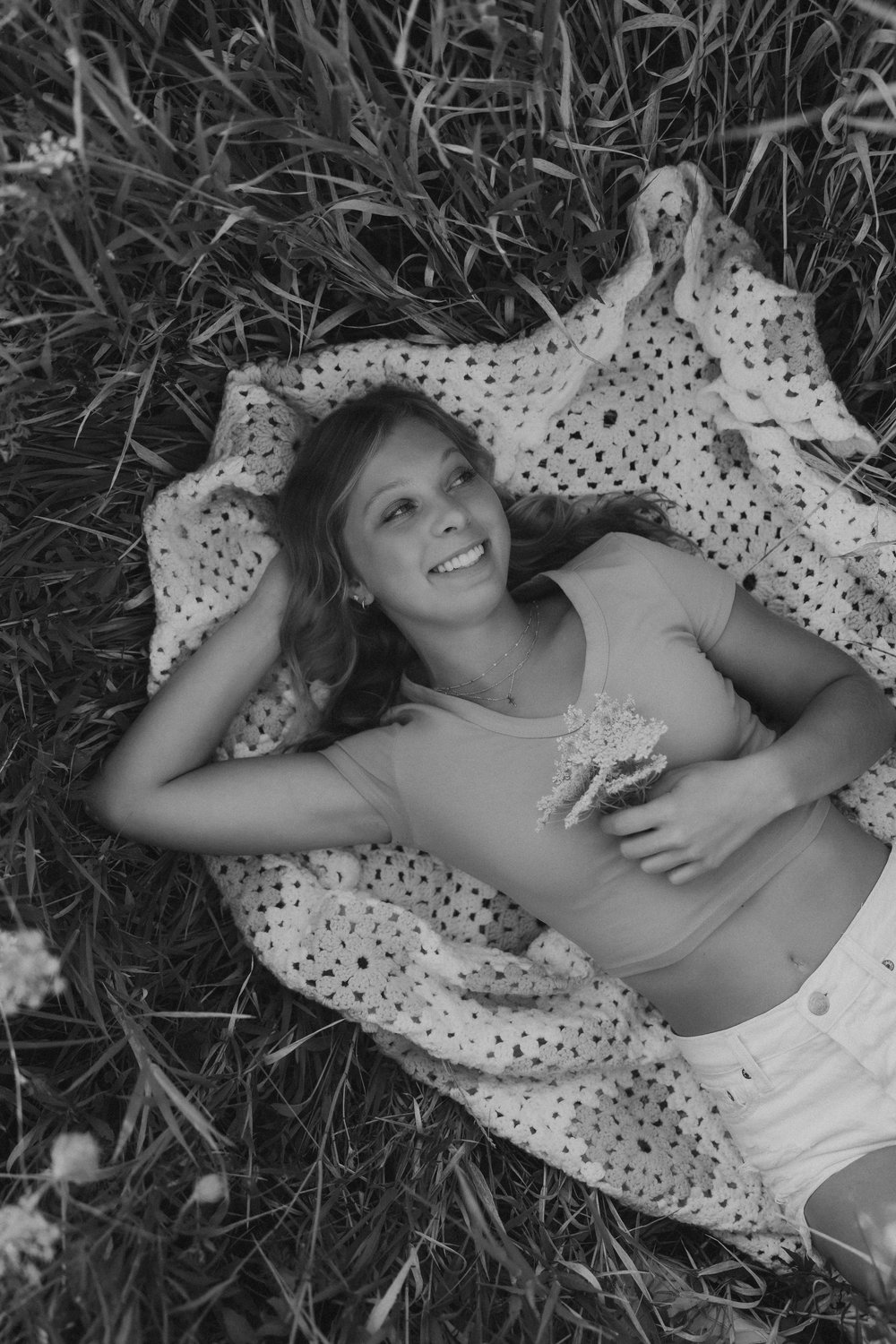  a black and white portrait of a high school senior laying on a crochet blanket in a field  