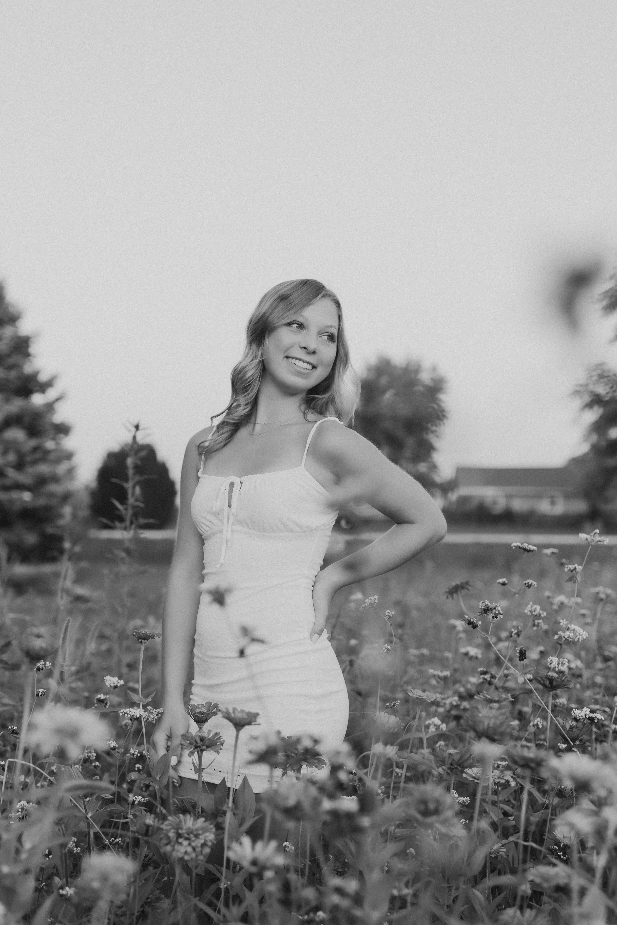  a black and white portrait of a young woman standing in a flower field  