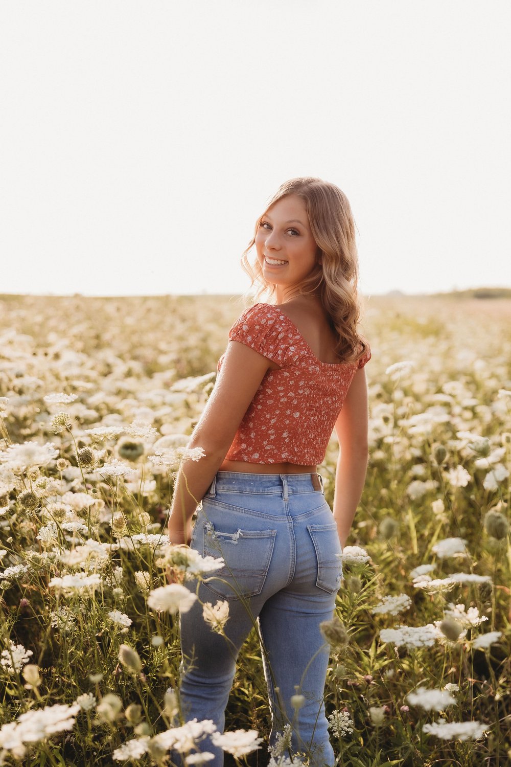  a young woman smiles over her shoulder in a patch of wildflowers 