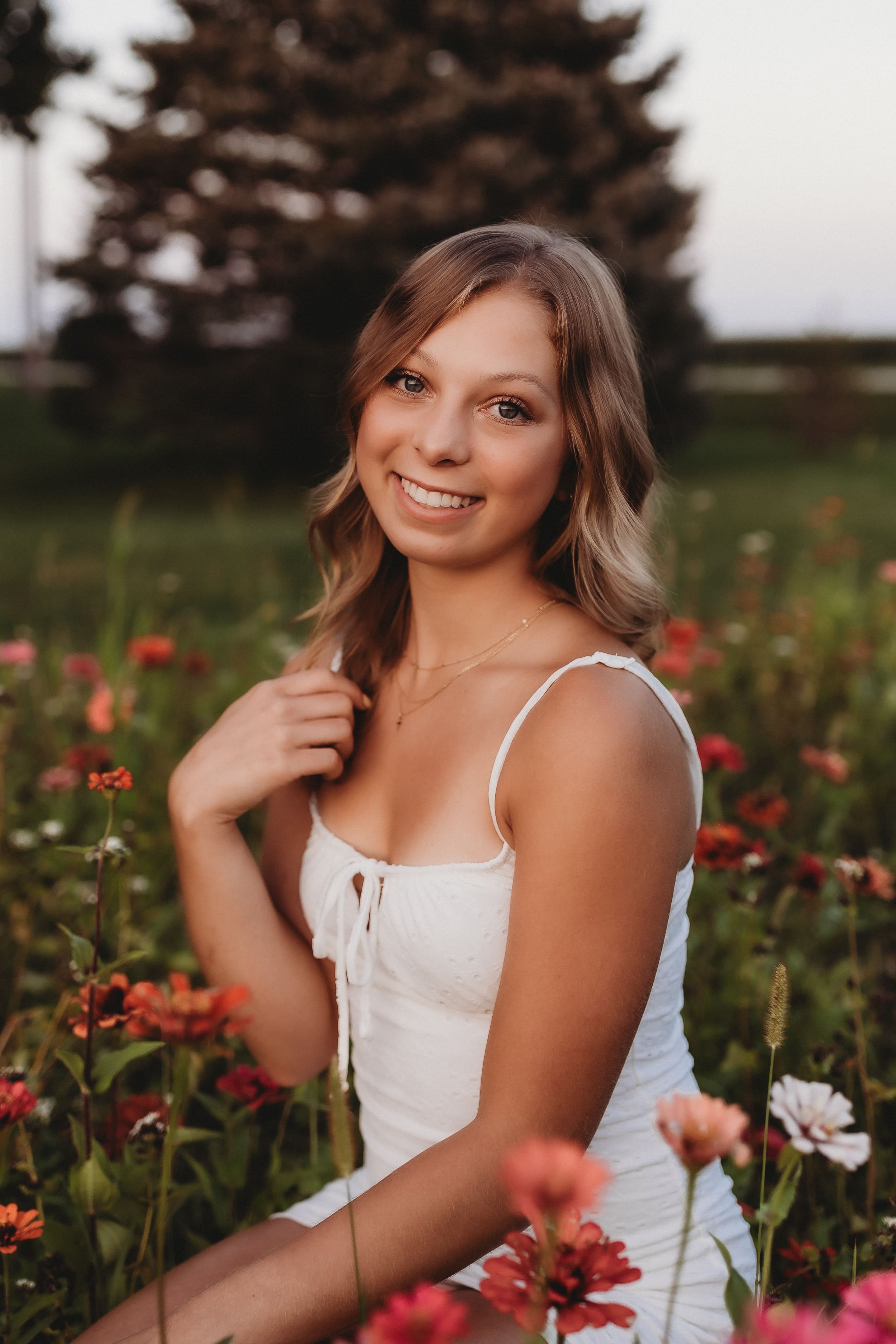  a senior photographer near me took this portrait of a young woman in a flower field with one hand on her knee and the other at her collarbone touching her hair 
