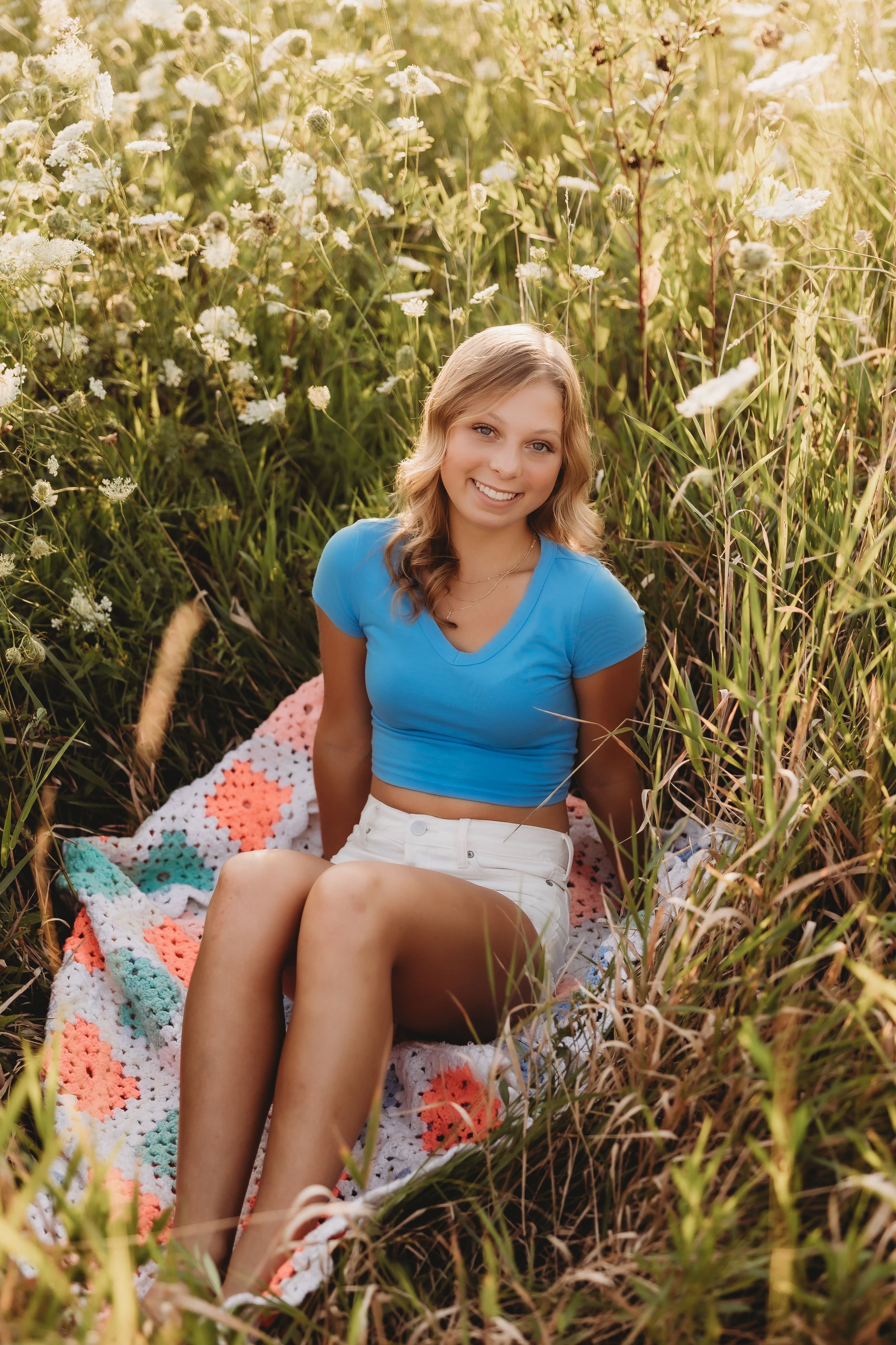  a senior photographer near me captured a young woman sitting on a crochet blanket in the middle of a flower field 