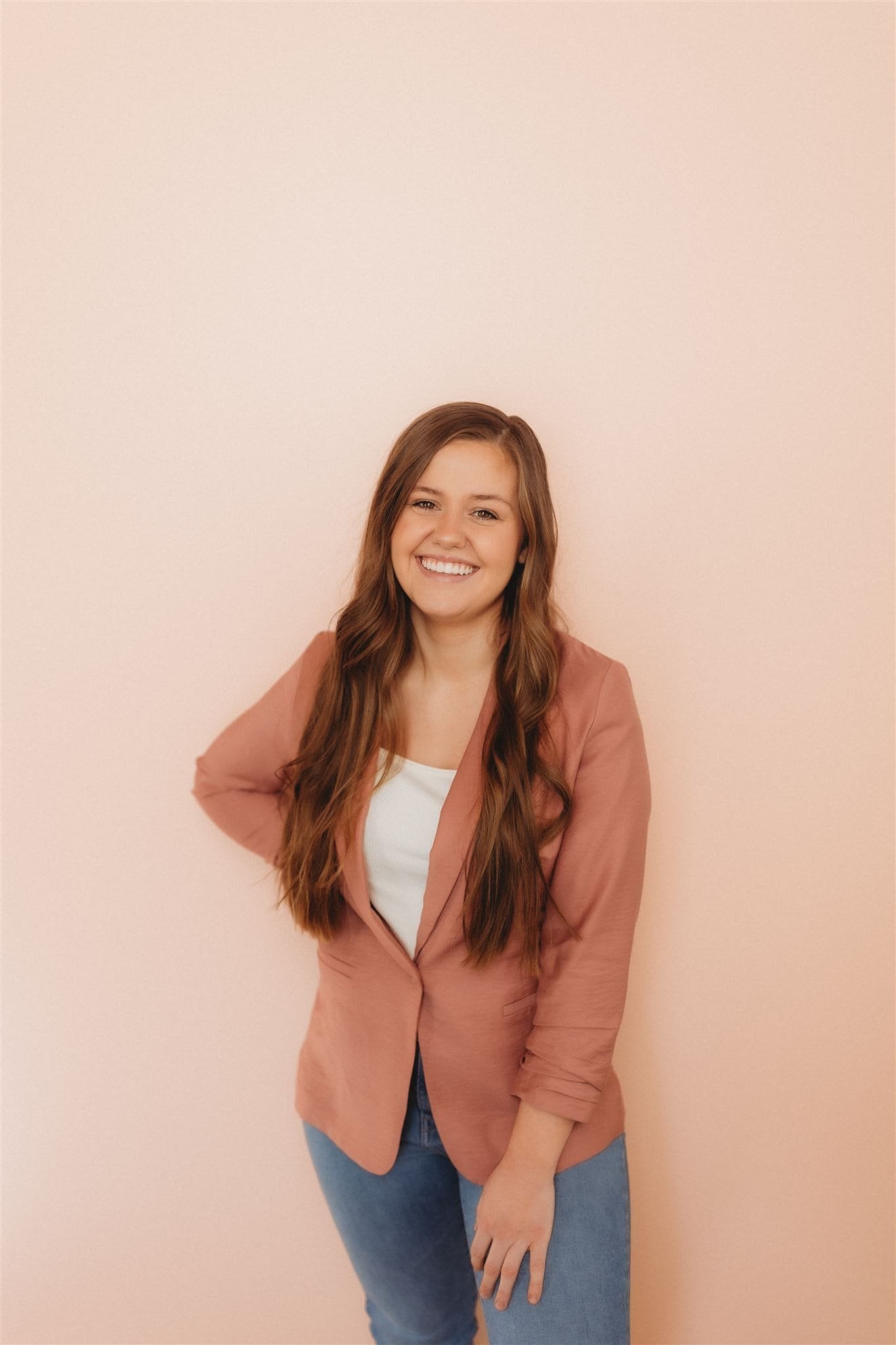  a woman wearing a pink blazer smiles in the studio with a headshot photographer 
