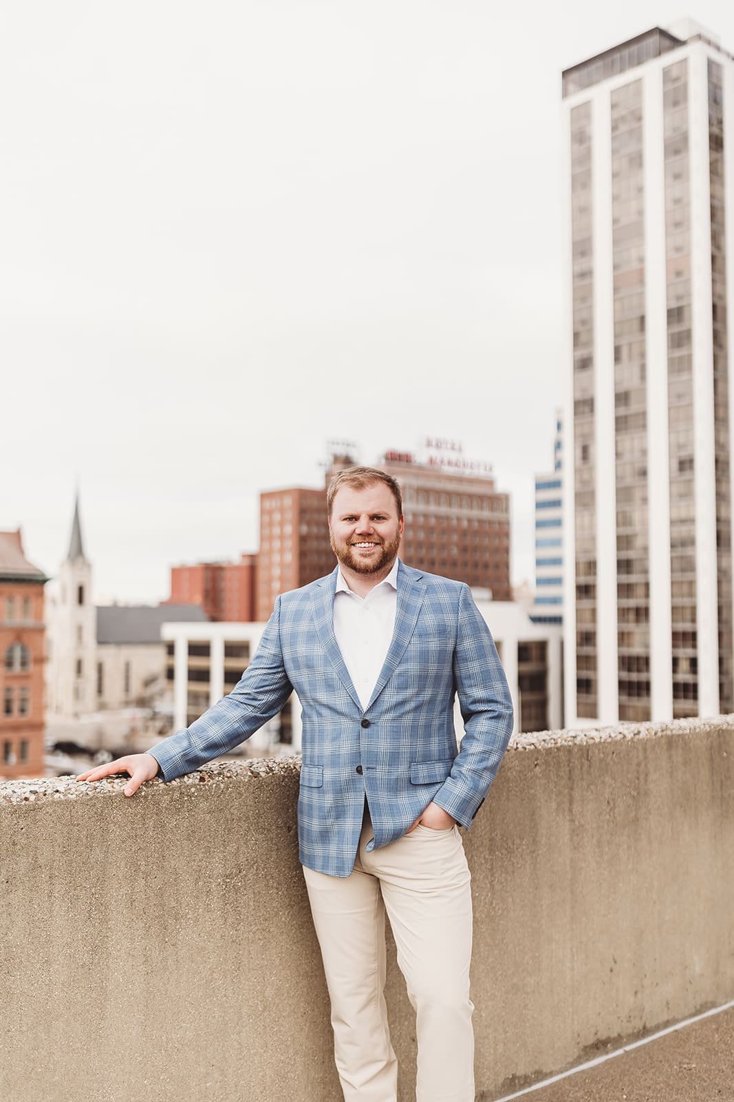  a man in a plaid suit jacket stands on a rooftop in downtown peoria for business headshots 
