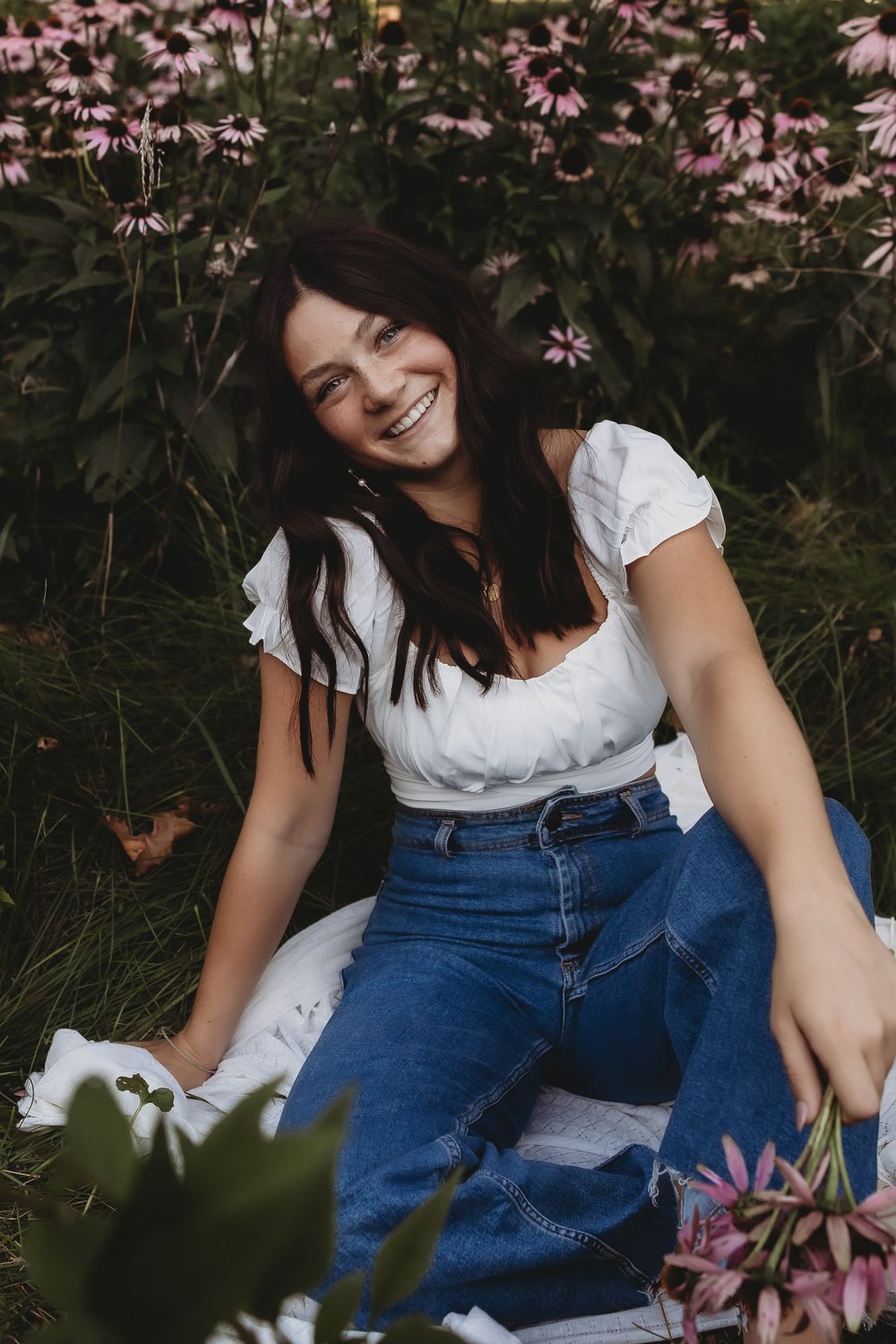  olivia smiles while sitting on a blanket in the grass in front of a bunch of growing flowers 