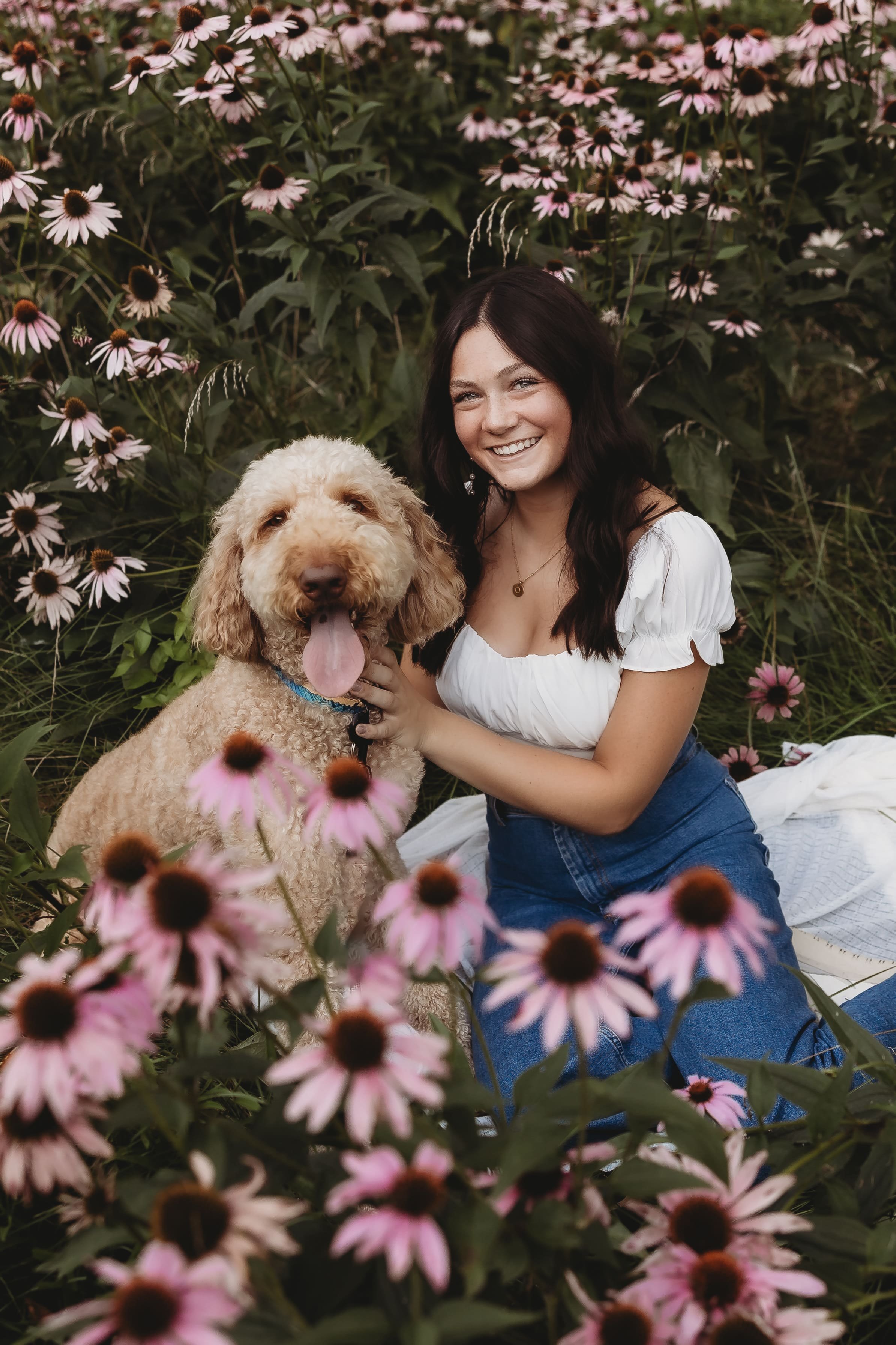  olivia and her dog post for senior pictures near me in a grassy pocket in the middle of a large bunch of flowers 