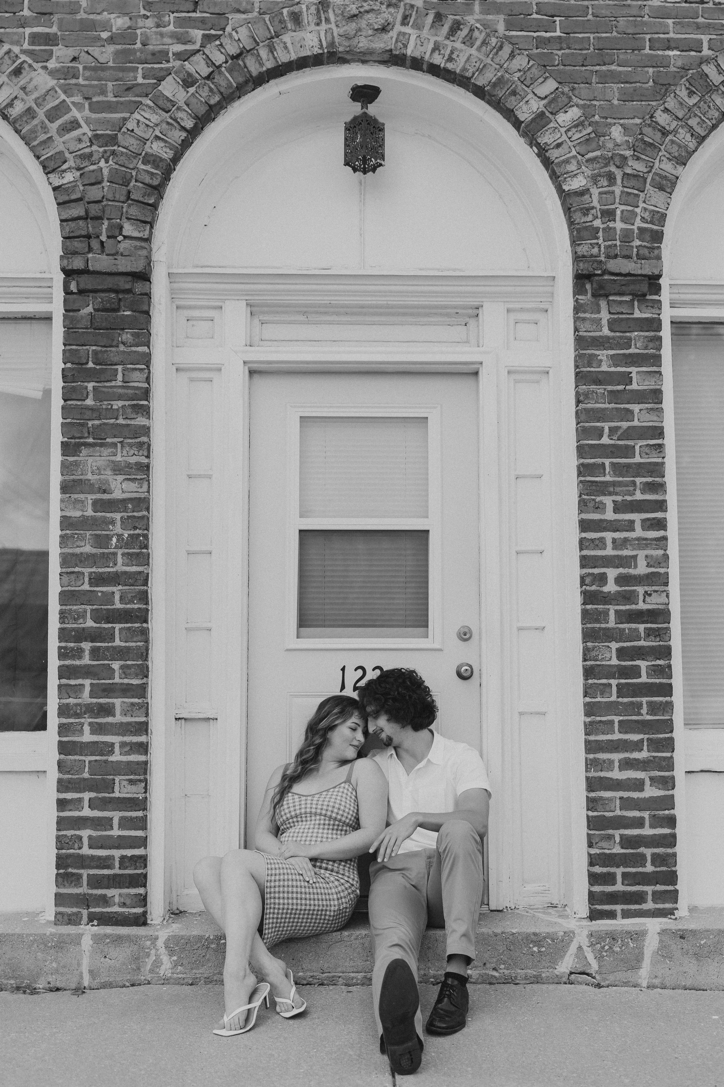  a couple lean their faces together while sitting on a stoop with their engagement photographer 