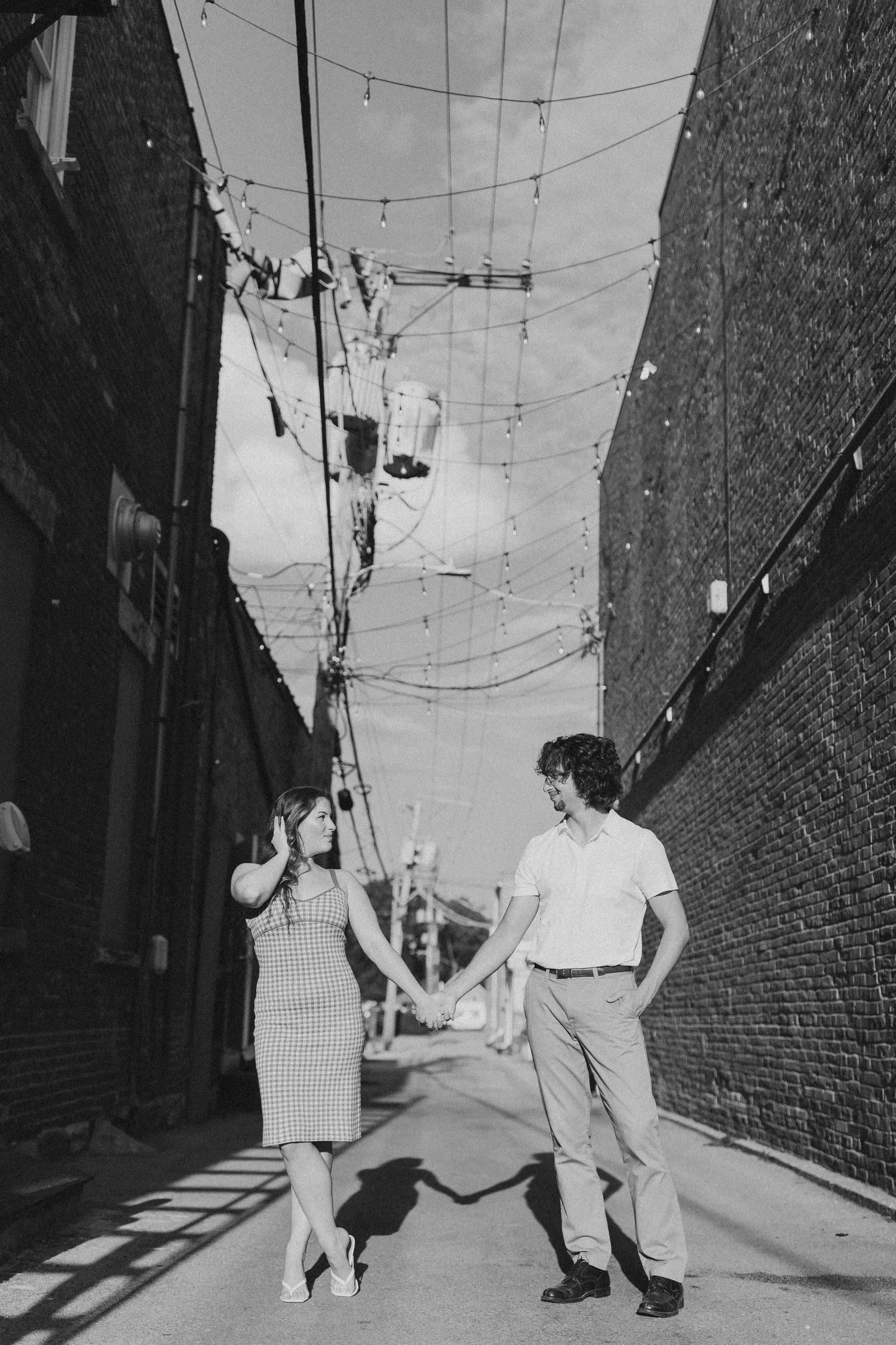  a couple stands in an alley looking at each other during their engagement photos 