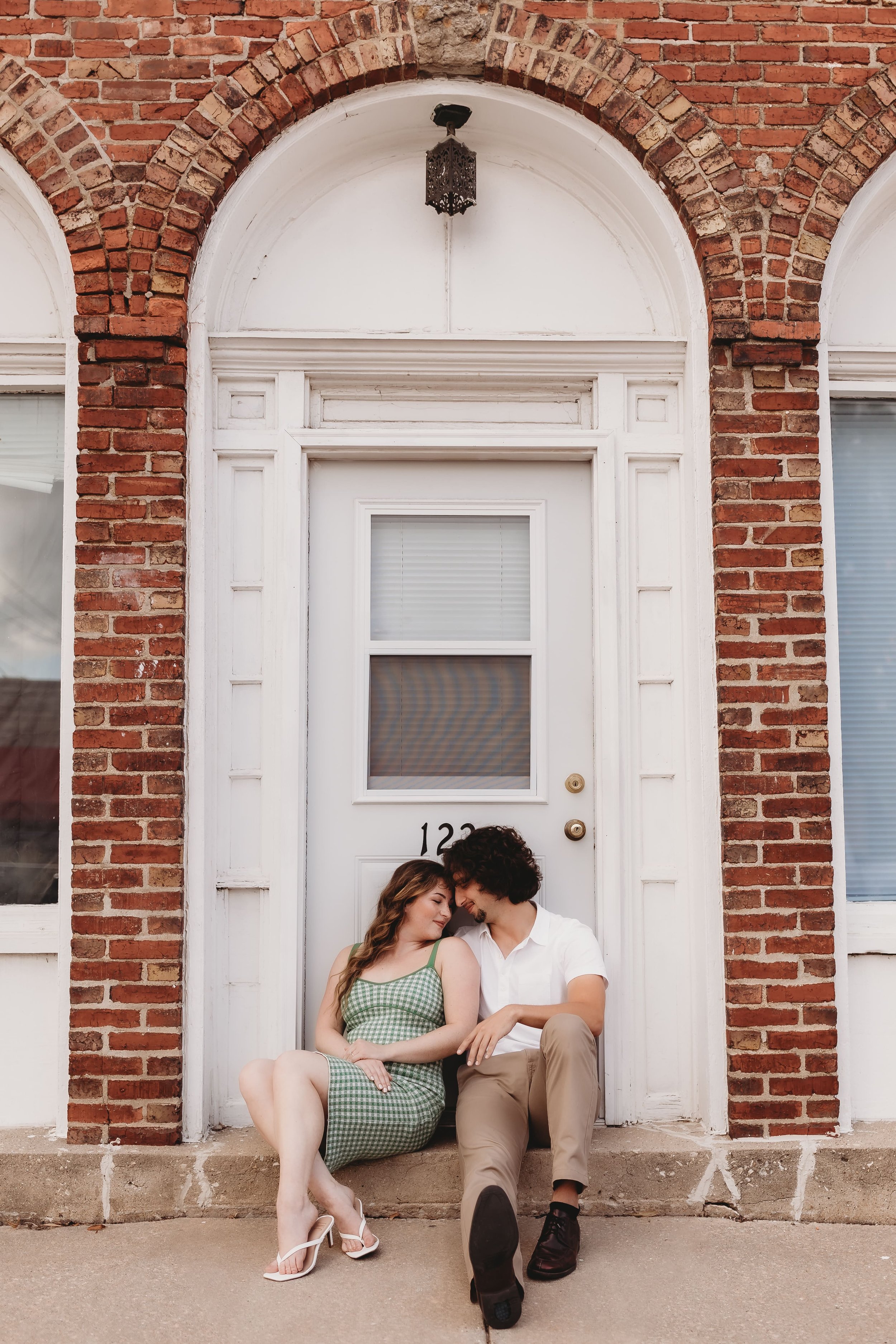  a couple lean their faces together while sitting on a stoop for their engagement photos 