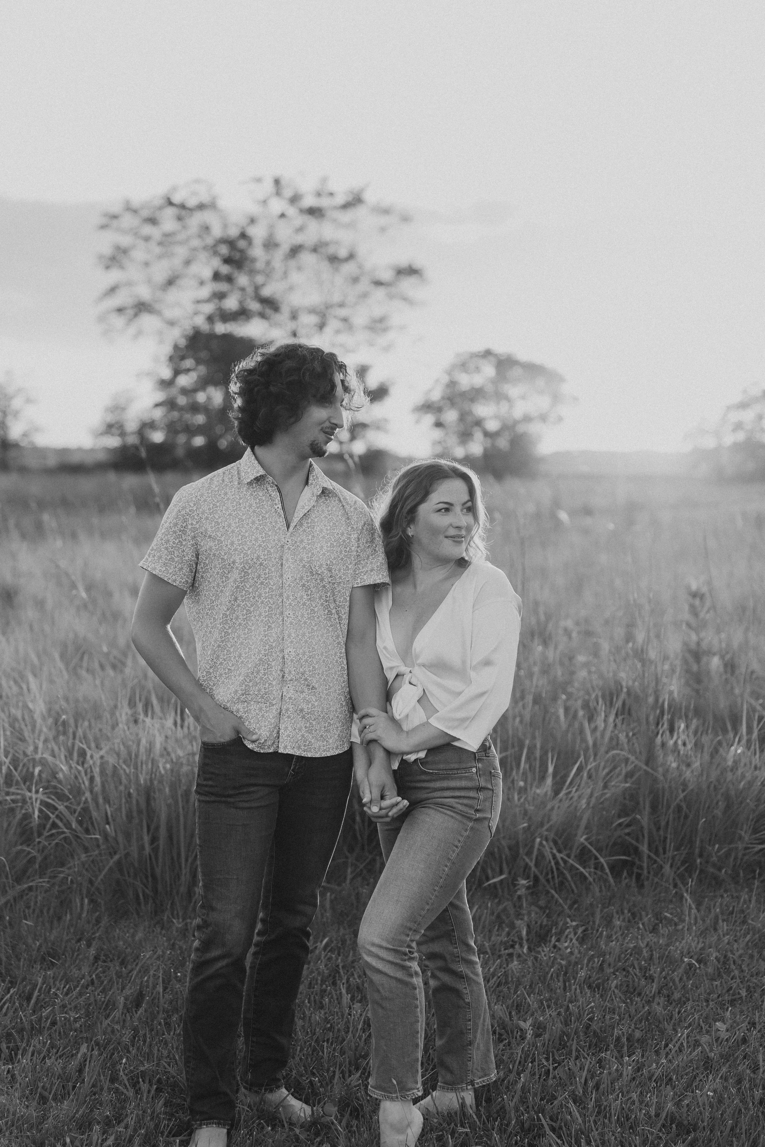  an engaged couple stand together and look to the side as they stand in a field during their engagement photos 