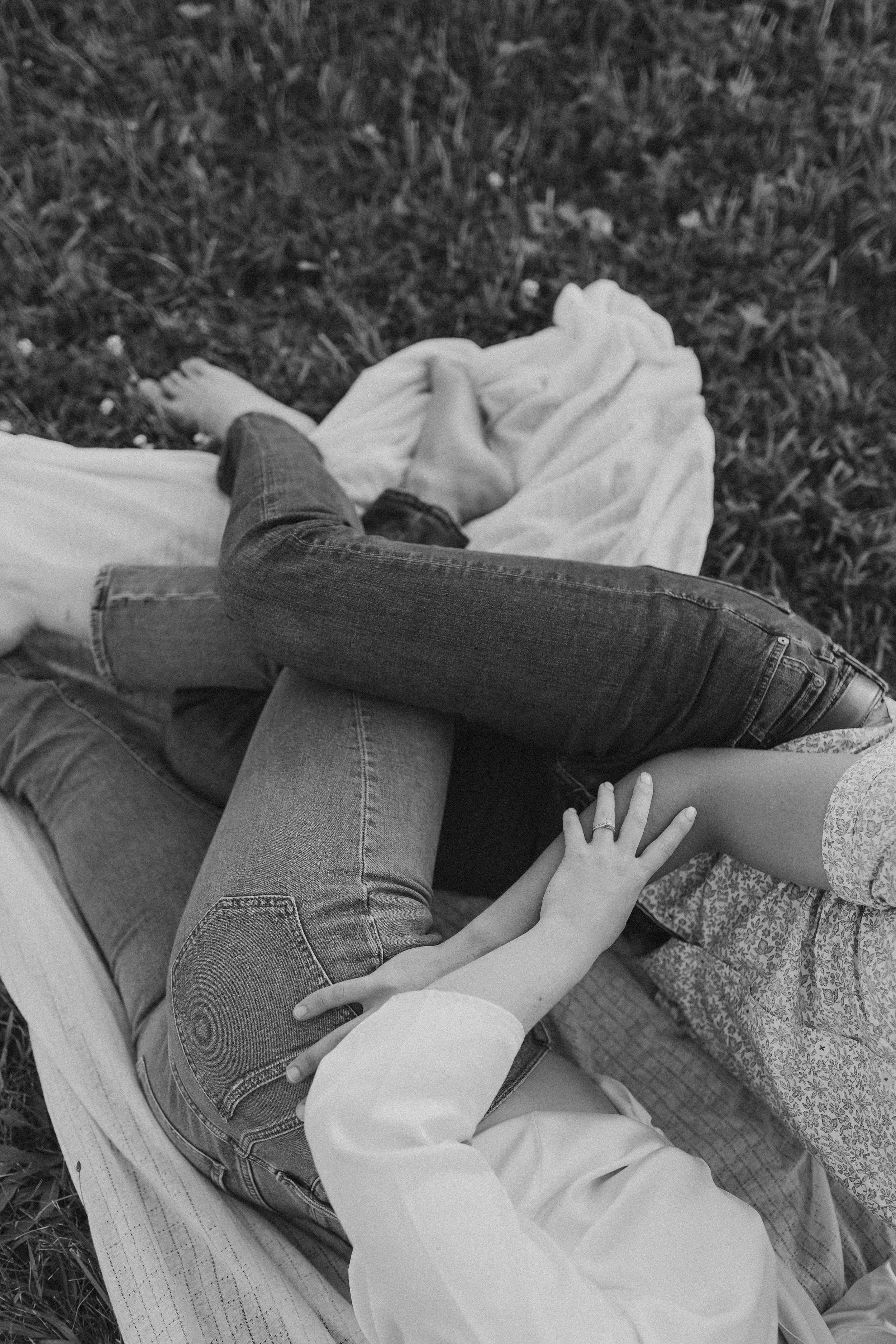  an engaged couple lay together on a picnic blanket with their legs intwined during their engagement photos  