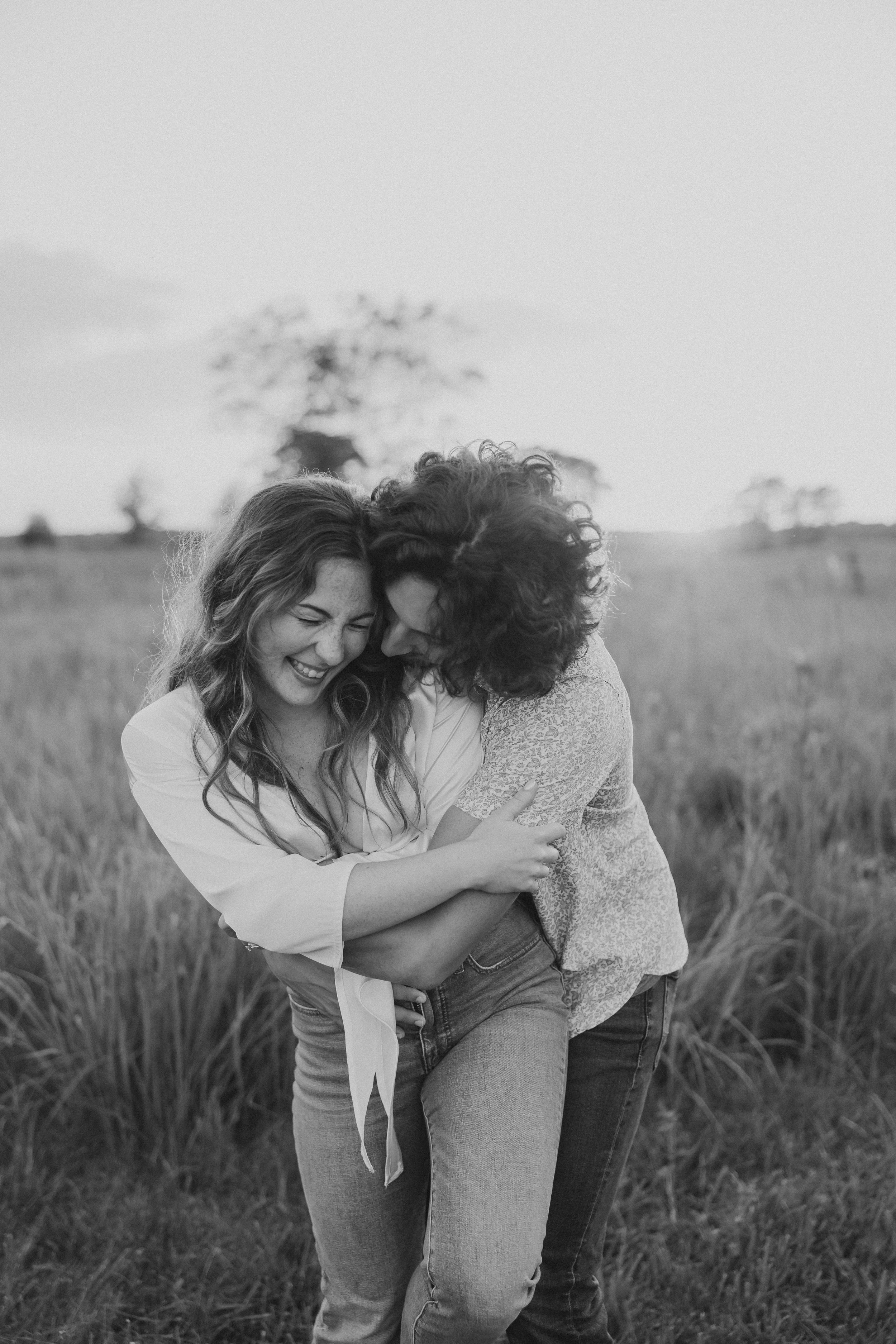 an engaged couple laugh as he hugs her from behind  