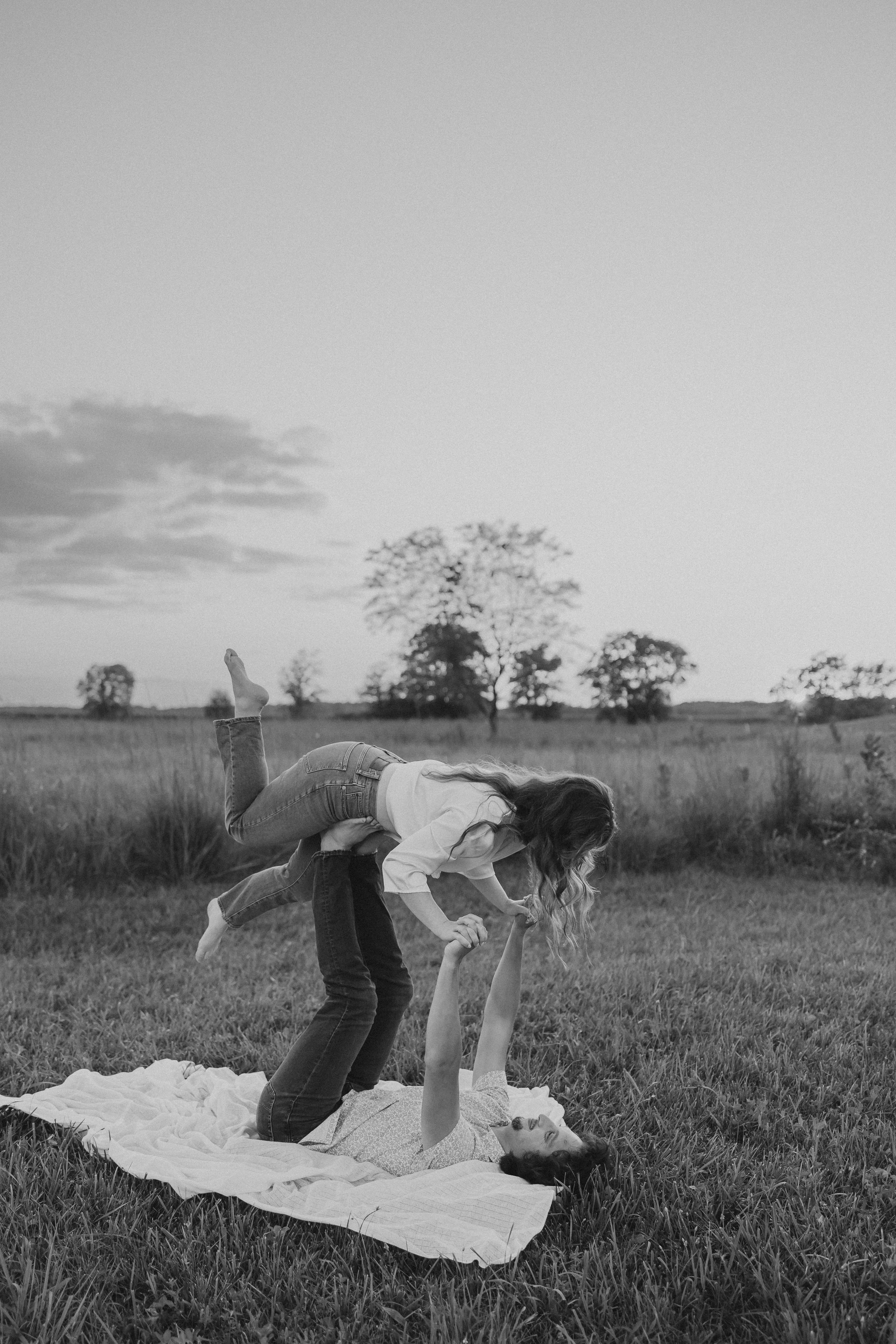  an engaged couple do the airplane on a picnic blanket in a field during their engagement photos 