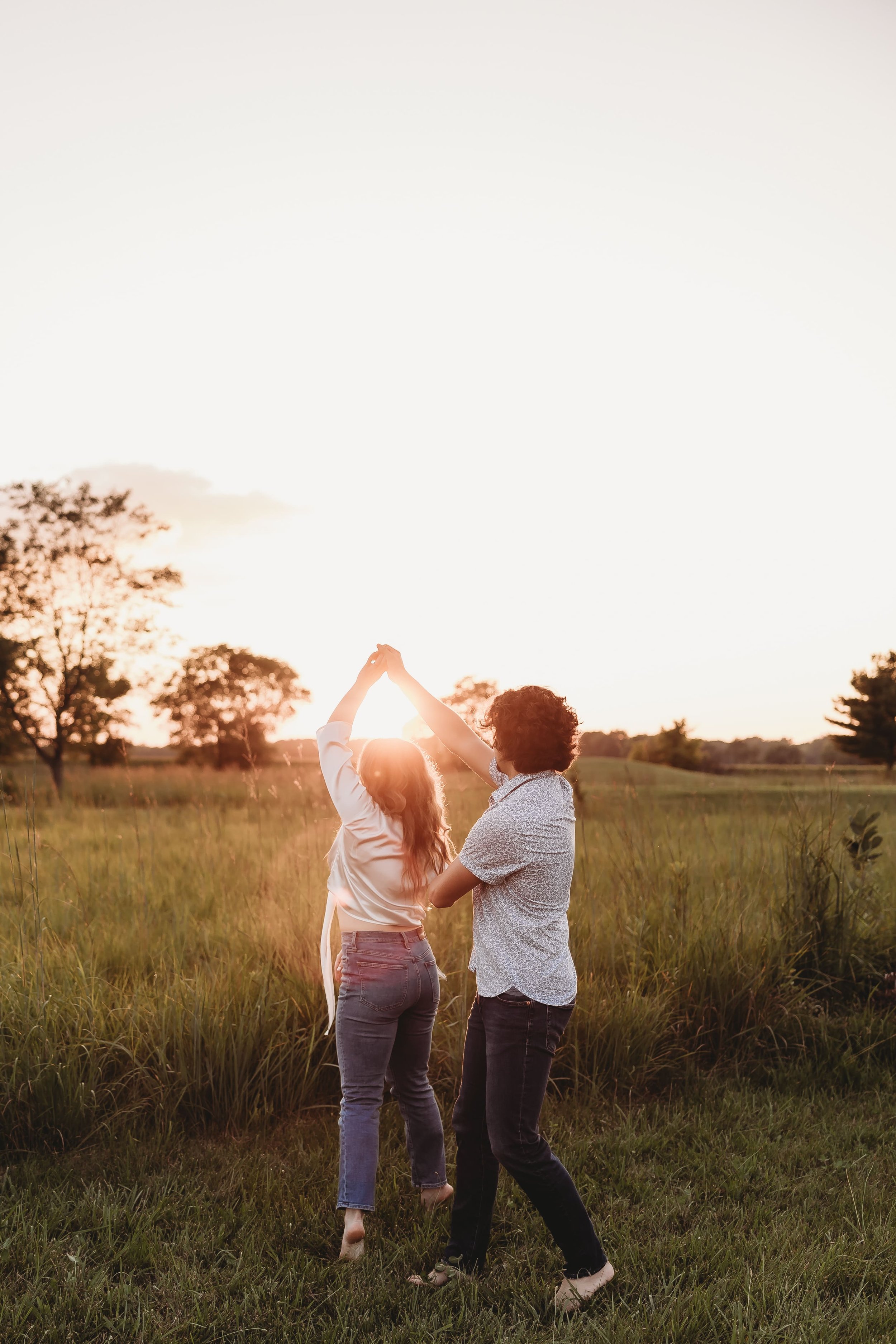  an engaged couple dance in a field as the sun sets 