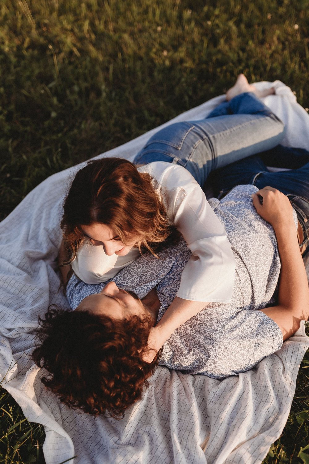  a couple lay together on a picnic blanket in a field during their engagement photos 