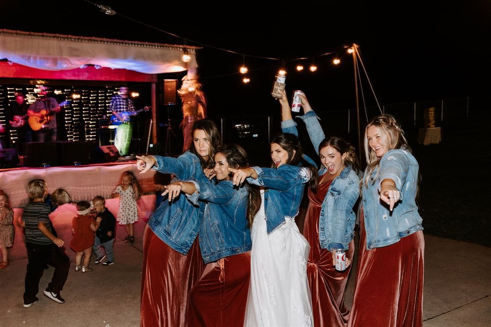  wedding recap, hannah and her bridesmaids all wearing jean jackets and pointing at something off camera during the reception 