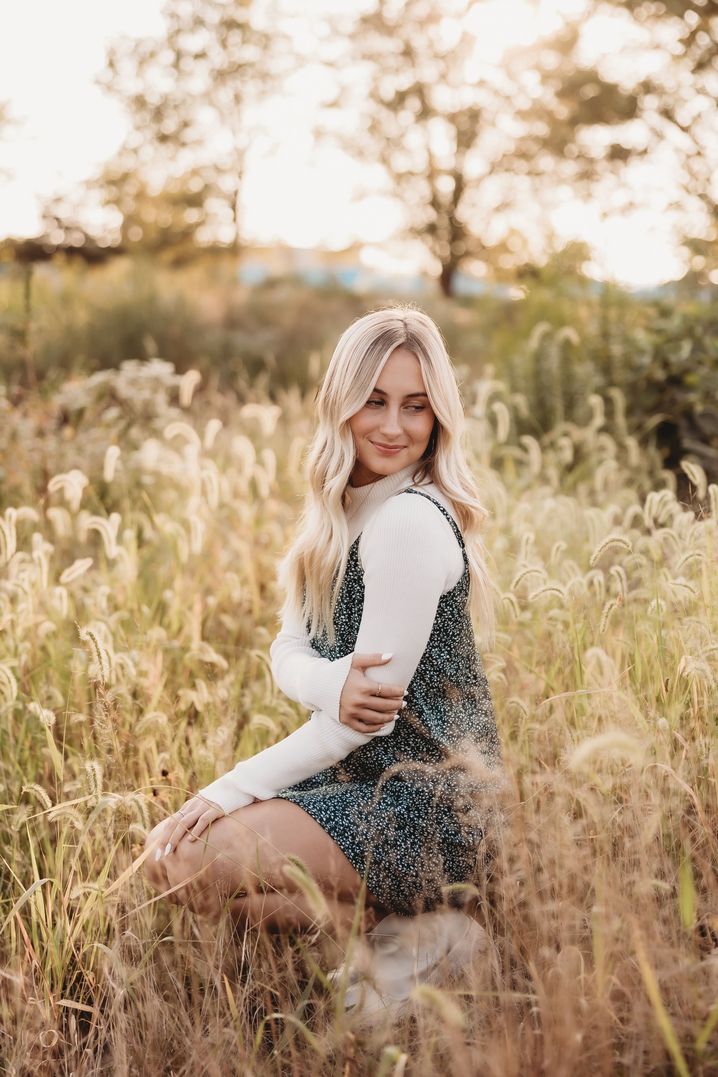  parker crouches down in a field as the sun sets behind her during her senior photos 