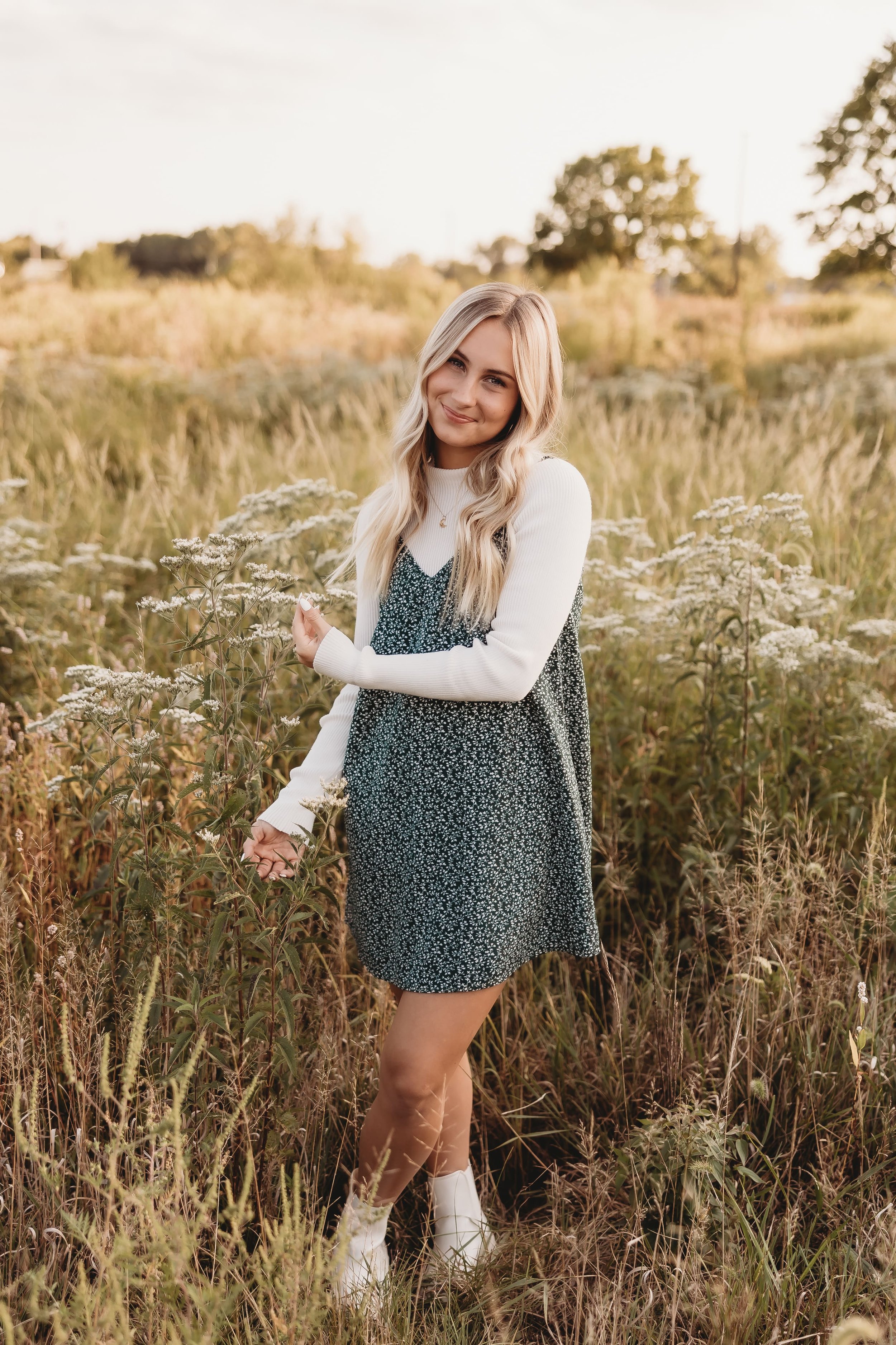  a young woman smiles in a field at golden hour for her senior photos 