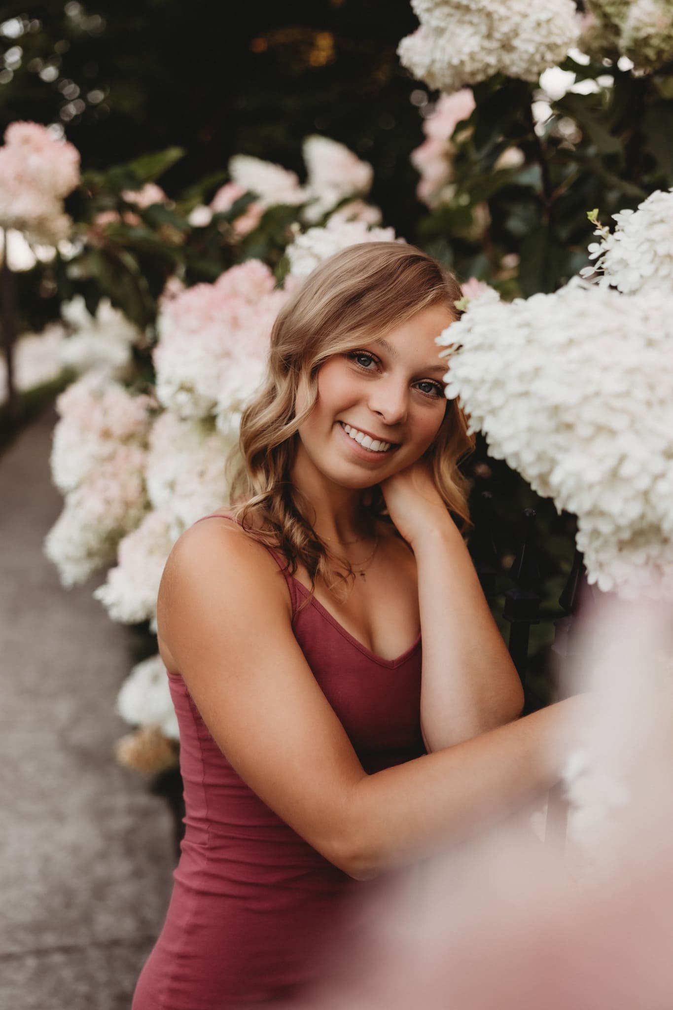  a girl smiles next to a fence of hydrangeas for senior photography 