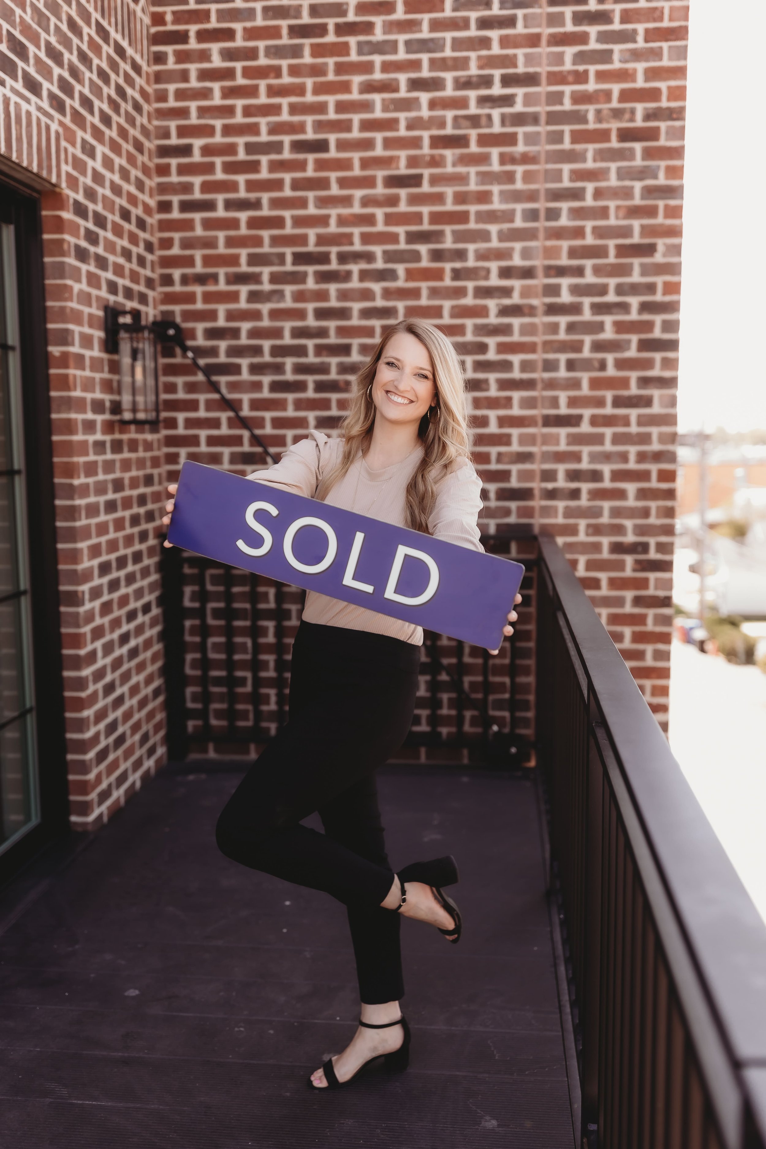  a woman smiles brightly while holding a for sale sign for a realtor branding photos session 