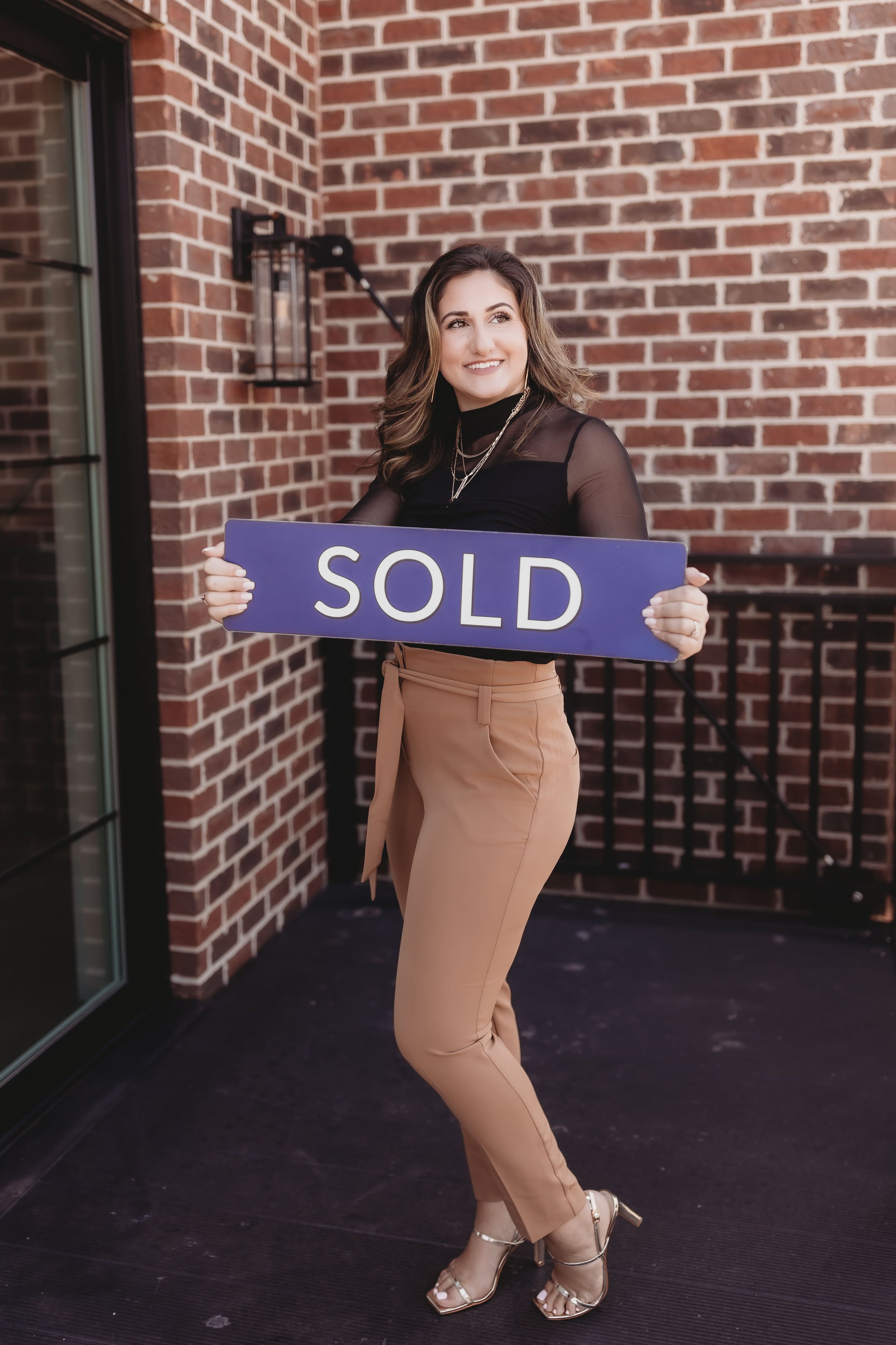  a woman smiles and looks to the side while holding a sold sign for realtor branding photos 