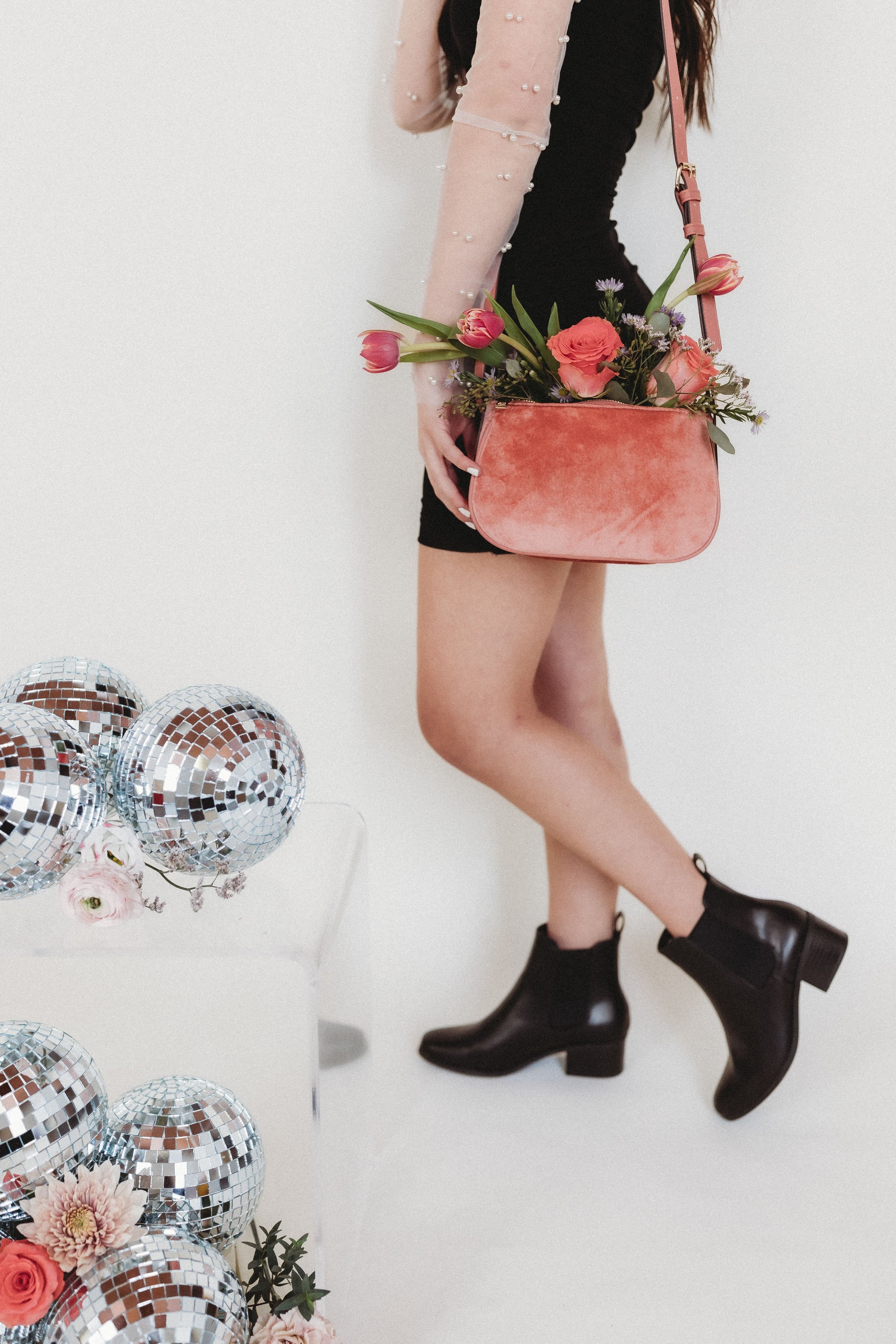  a woman stands with purse full of flowers next to an arrangement of flowers and disco balls 