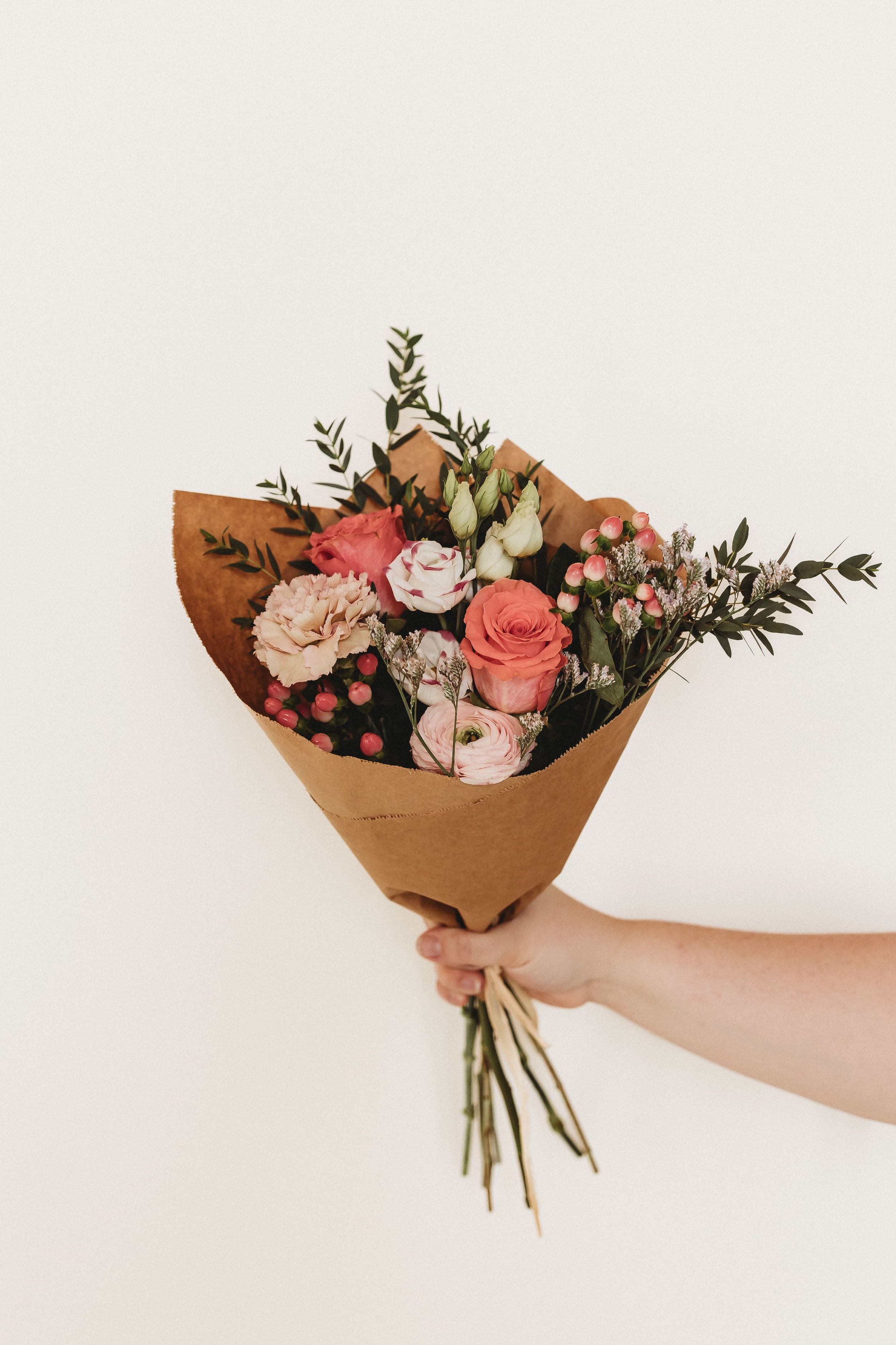  an arm holds out a hand tied bouquet of flowers wrapped in brown paper for business branding photography 