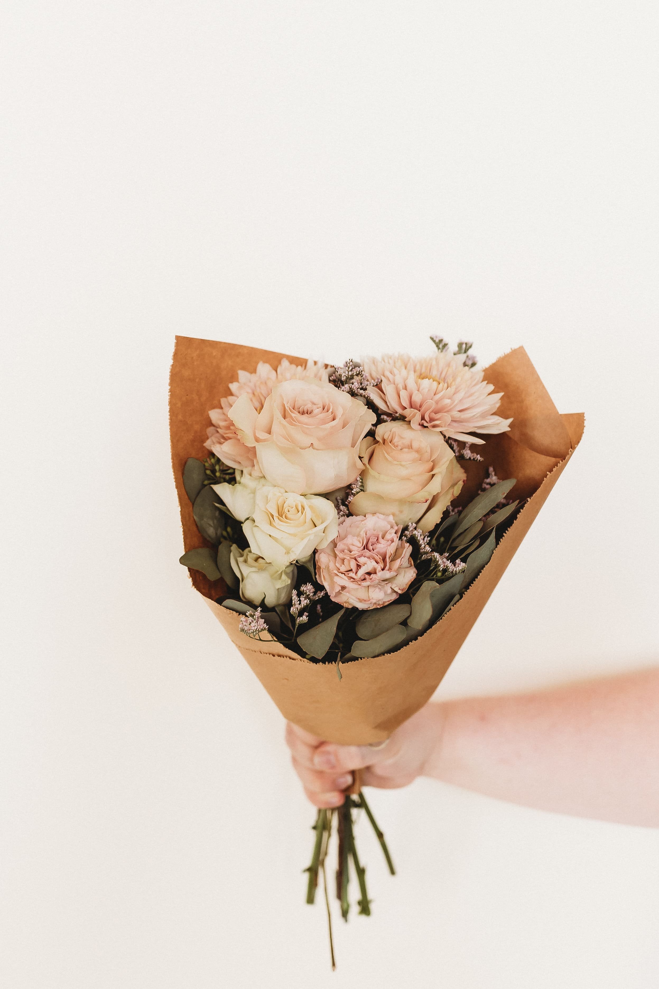  an arm holds out a bouquet of flowers against a white backdrop 