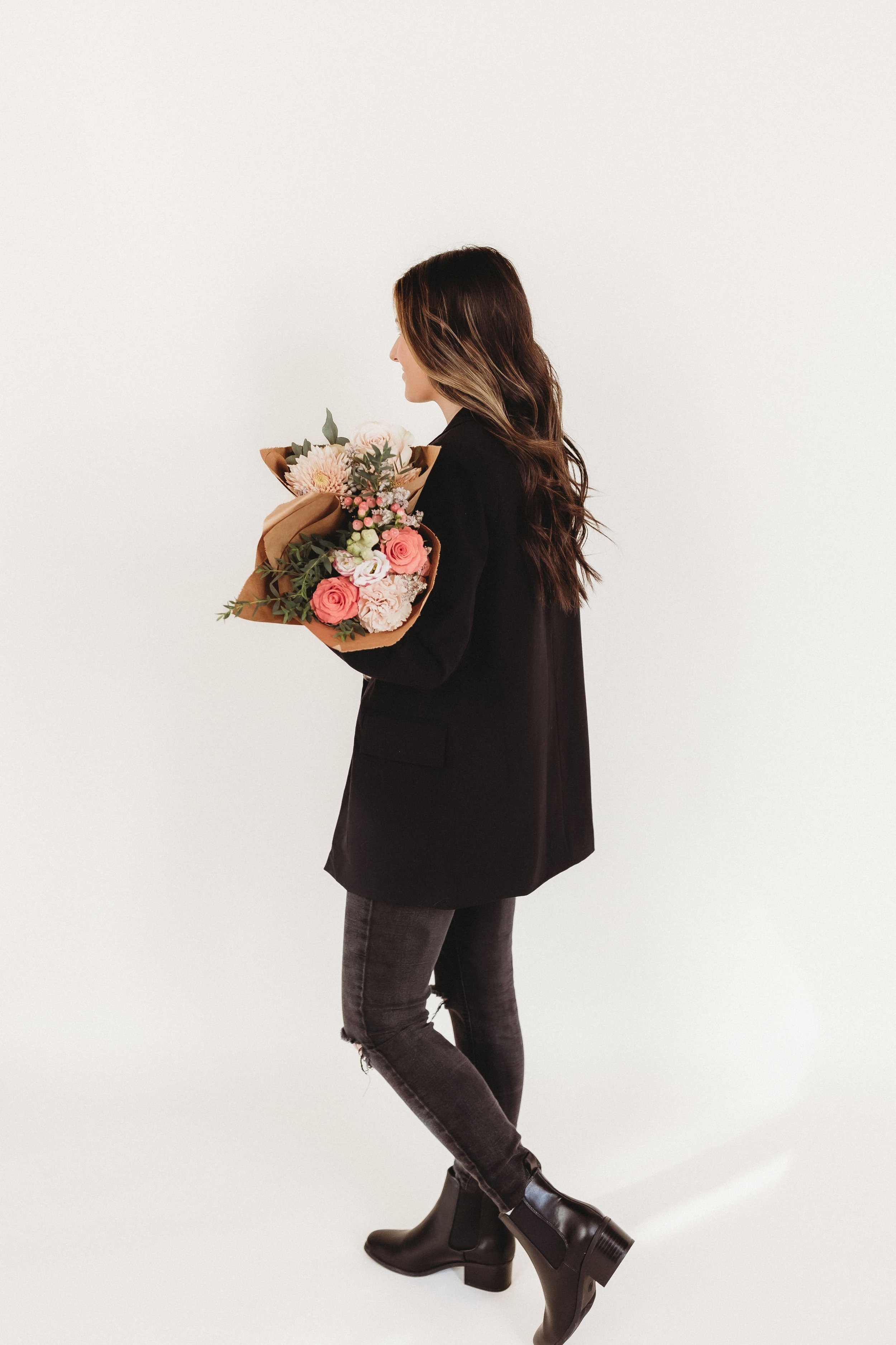  a woman walks while holding a bouquet of flowers and wearing all black 
