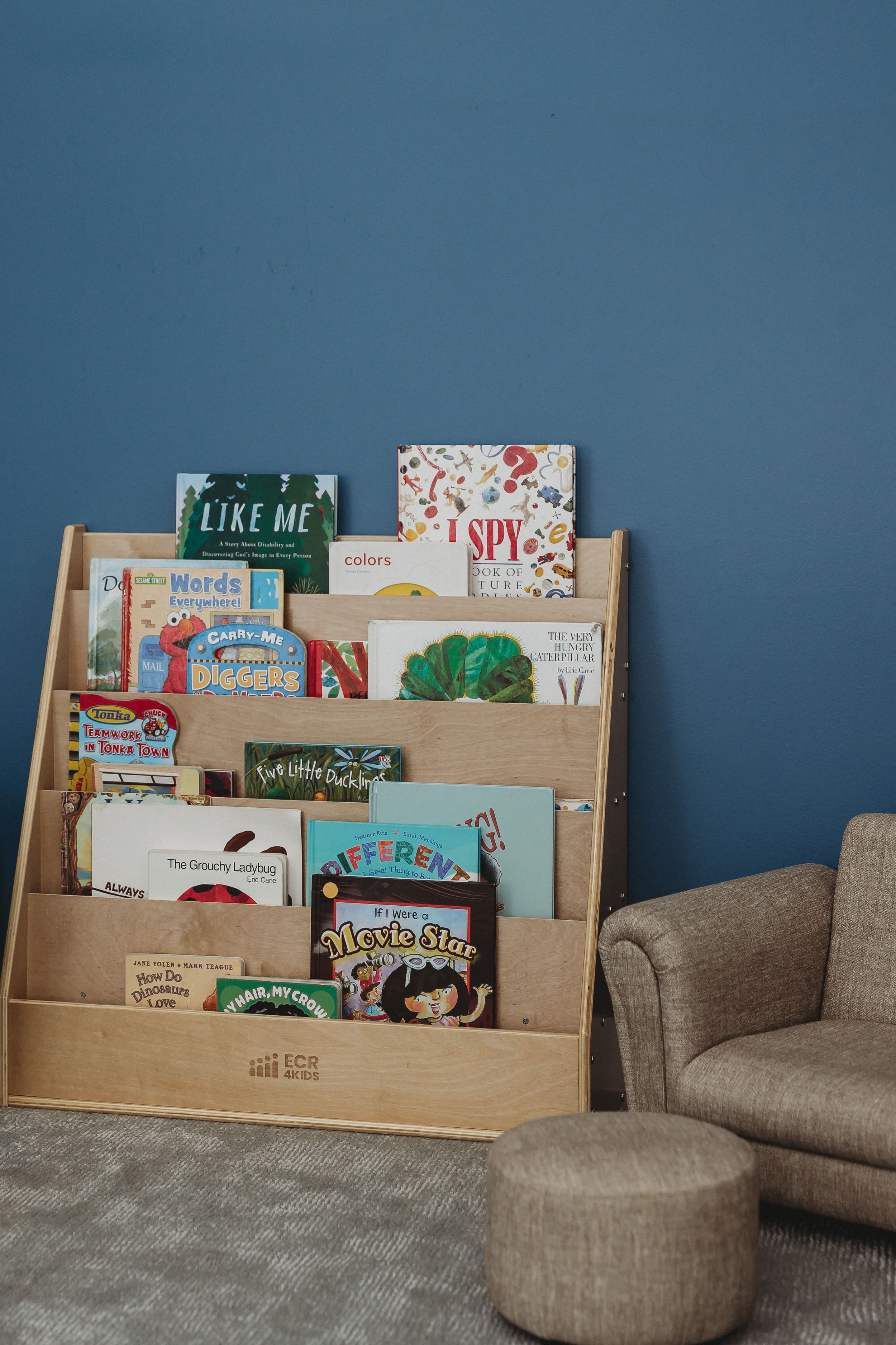  a small bookcase with children’s books stands next to a child size chair and footstool 