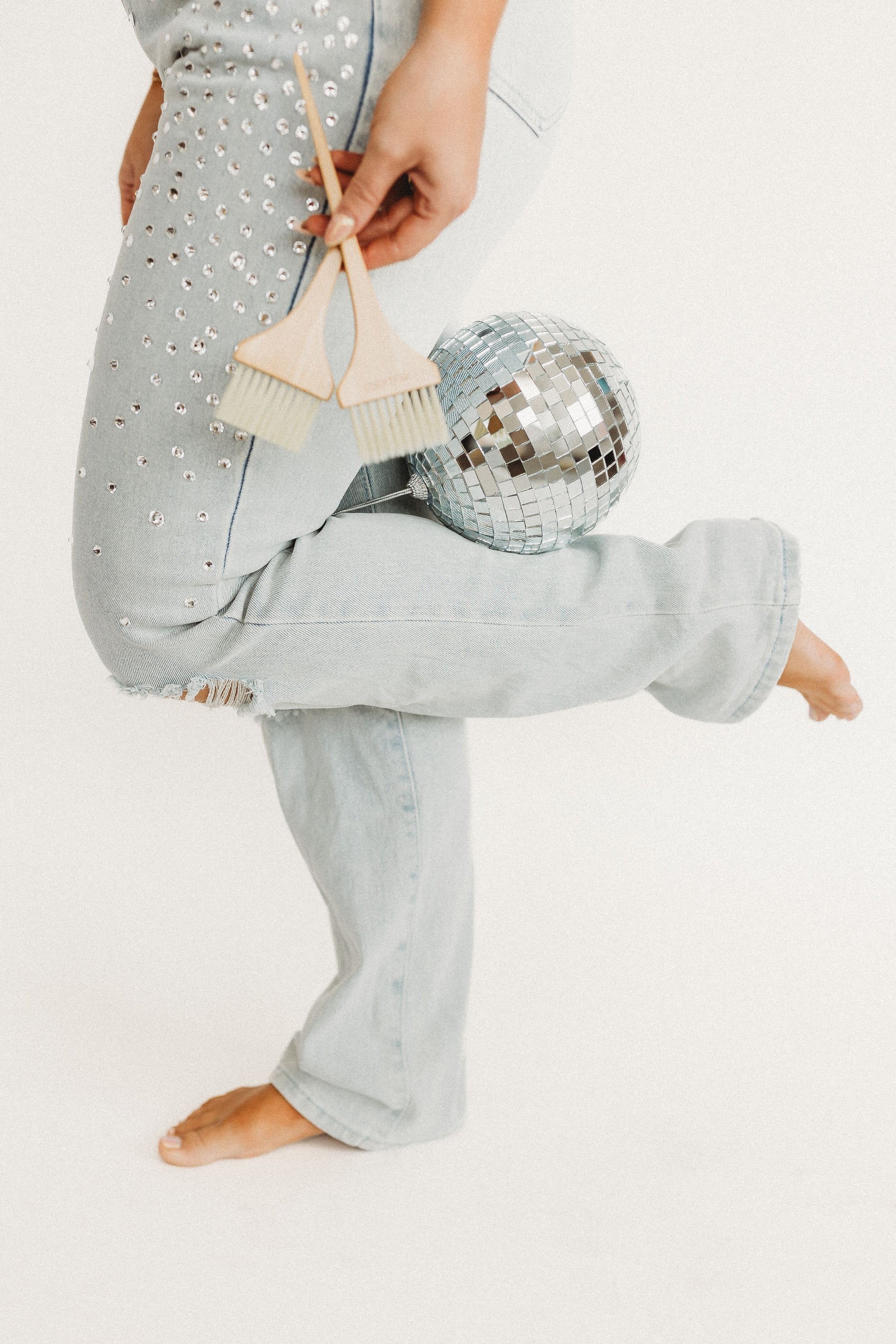  a woman kicks up her leg and holds a disco ball with two color brushes in her hand 